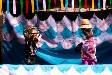 Bonecos teatrais em cena com fundo decorado em azul e branco simulando água.