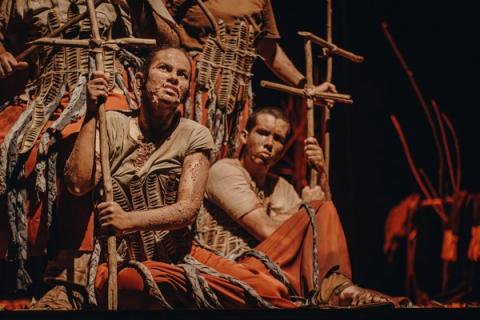 Grupo de atores sentados com cruzes nas mãos.