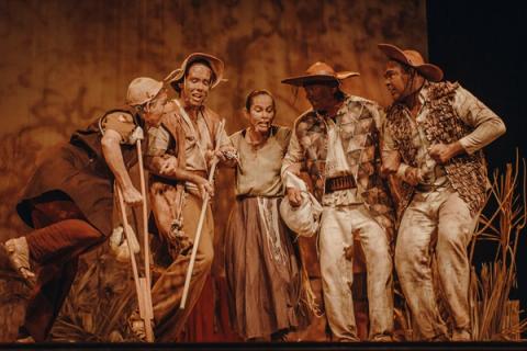 Grupo de atores em cena teatral, vestidos com roupas tradicionais nordestinas e chapéus.