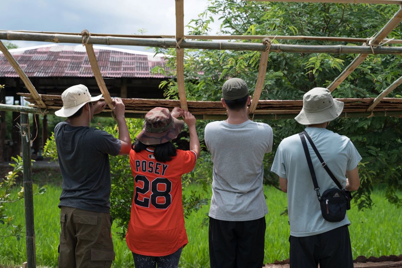 Participants working together on a bamboo and leaf roof