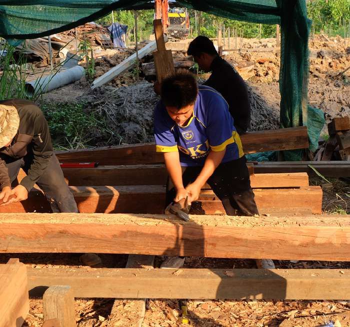 People hand-planing timber beams together on a building site