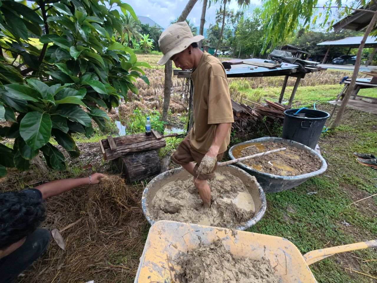 A participant mixing earth and straw in a basin outdoors