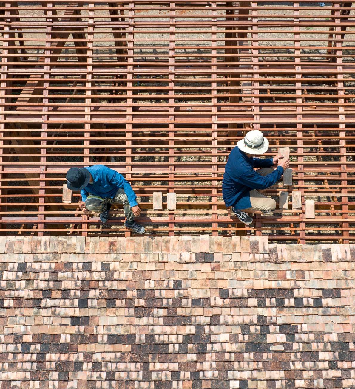 Two craftsmen working on a timber lattice above brick walls