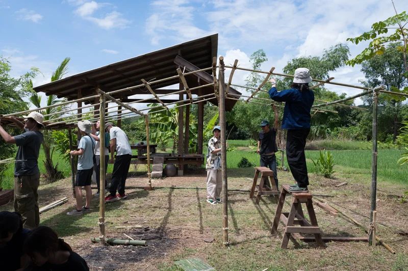 Participants building a simple timber shelter beside the pavilion