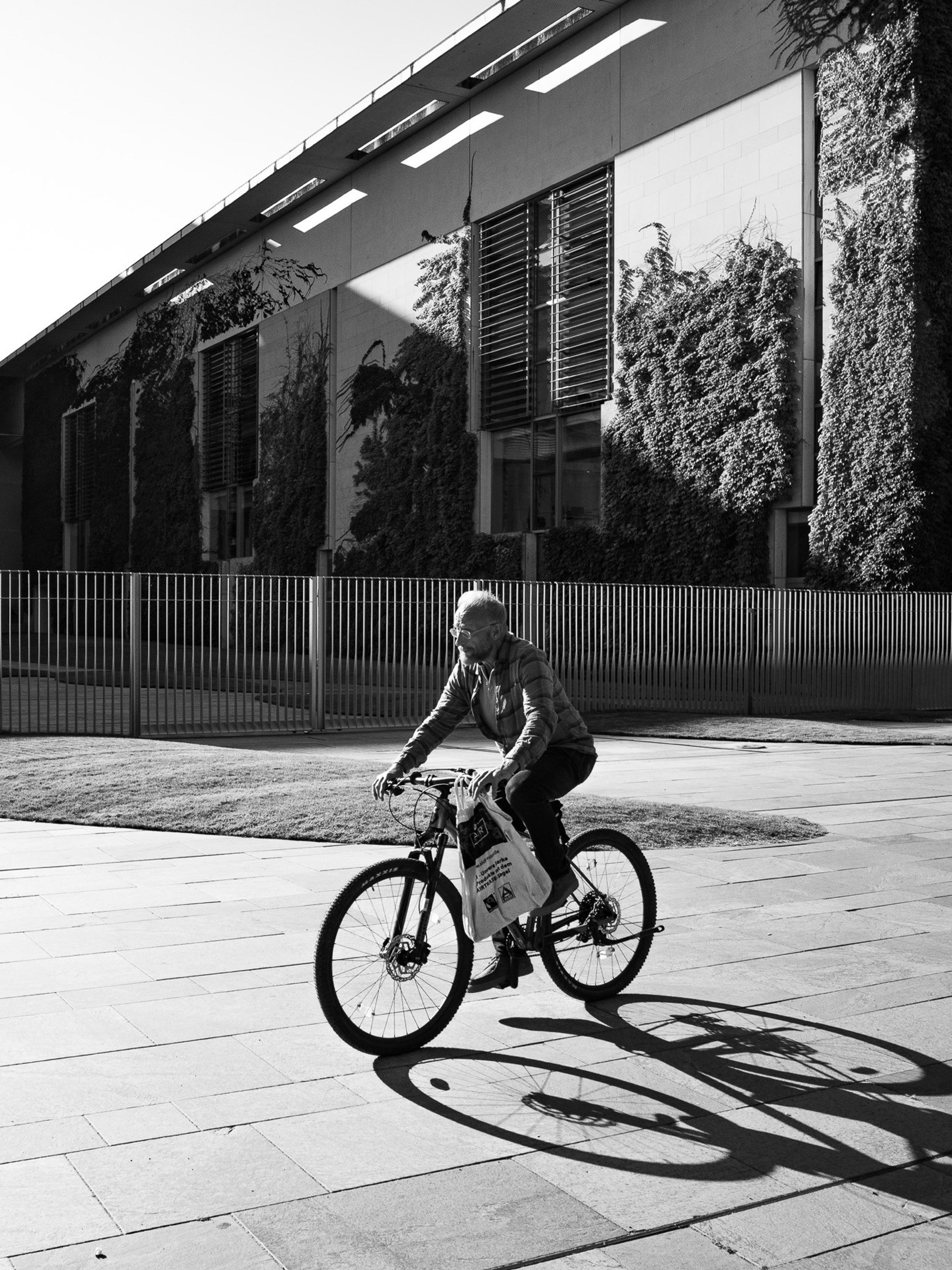 Black and white shot of a cyclist casting a long shadow in front of a modern building with green walls