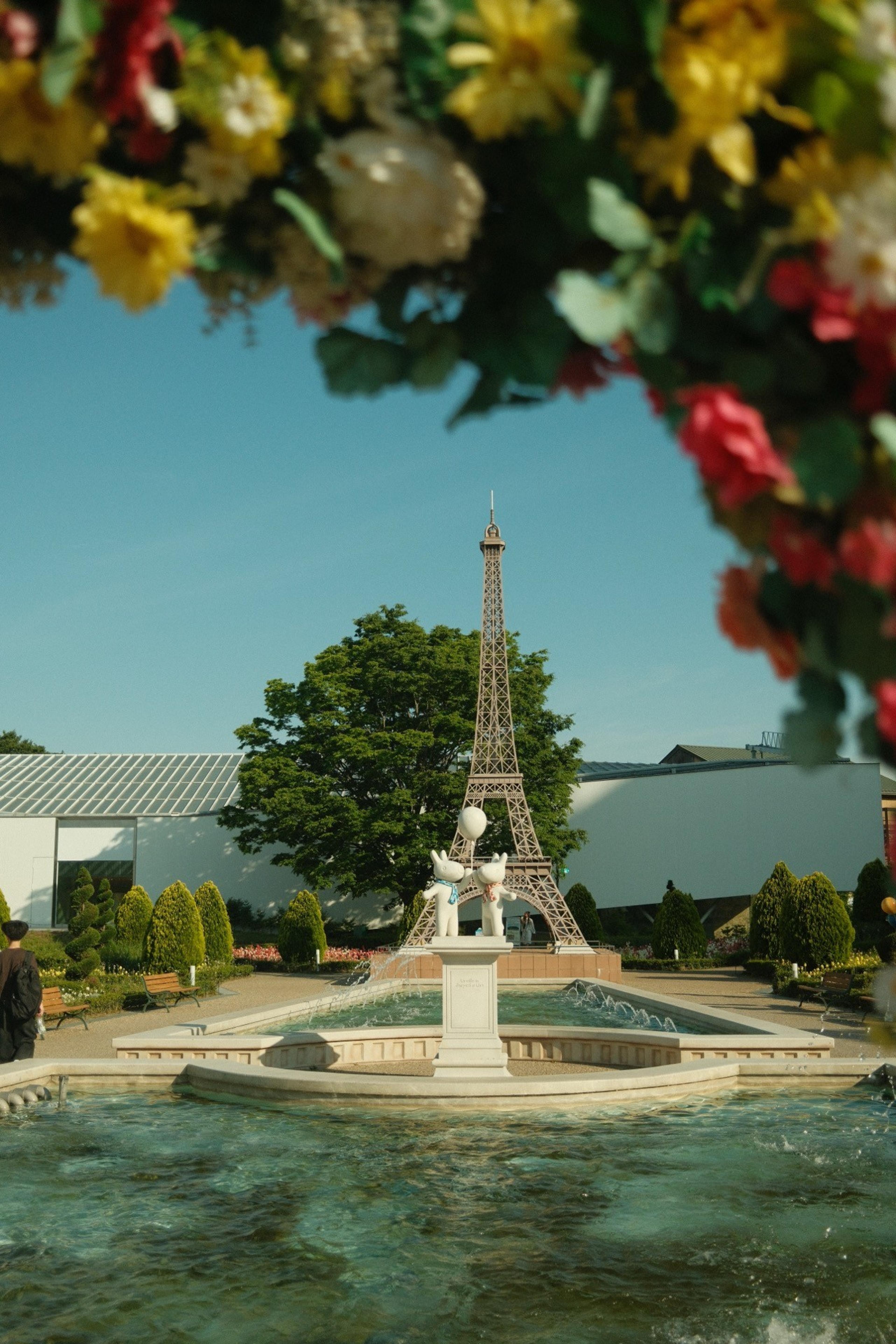 Fountain with a small Eiffel Tower replica and bunny statues, framed by hanging flowers