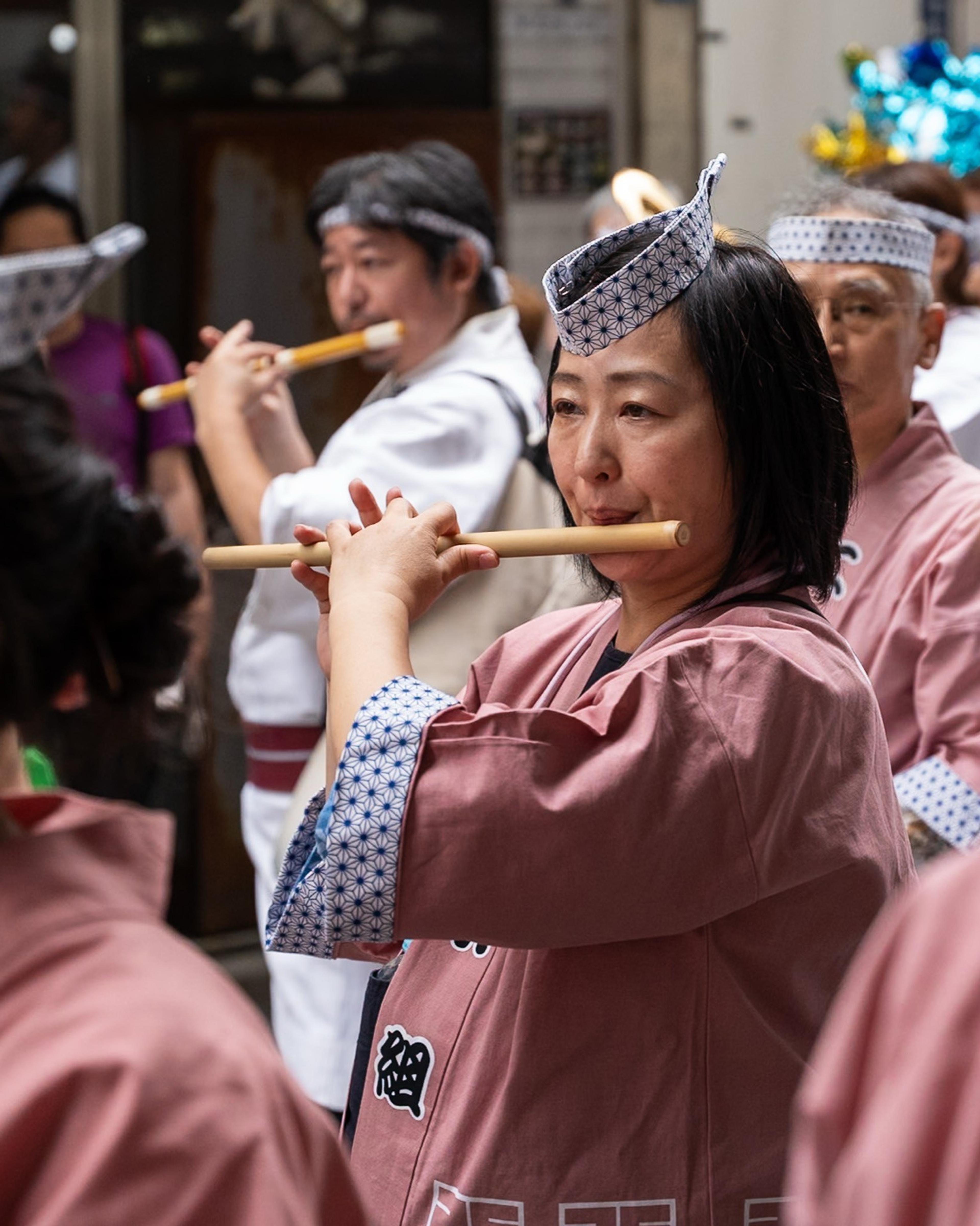 Festival musicians in pink happi coats and patterned headbands playing bamboo flutes