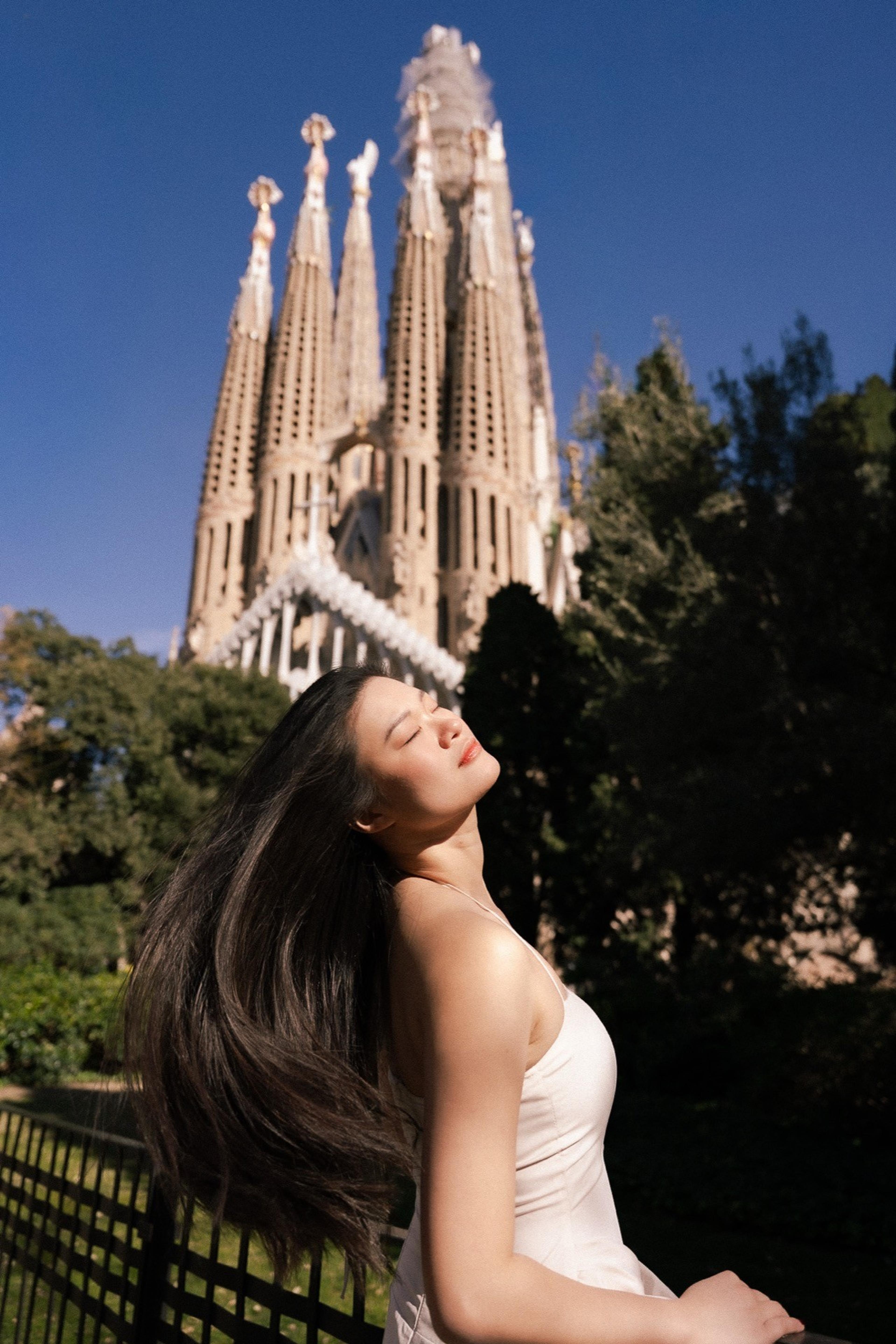 Woman tossing her long hair in the sun with the spires of a towering basilica behind her