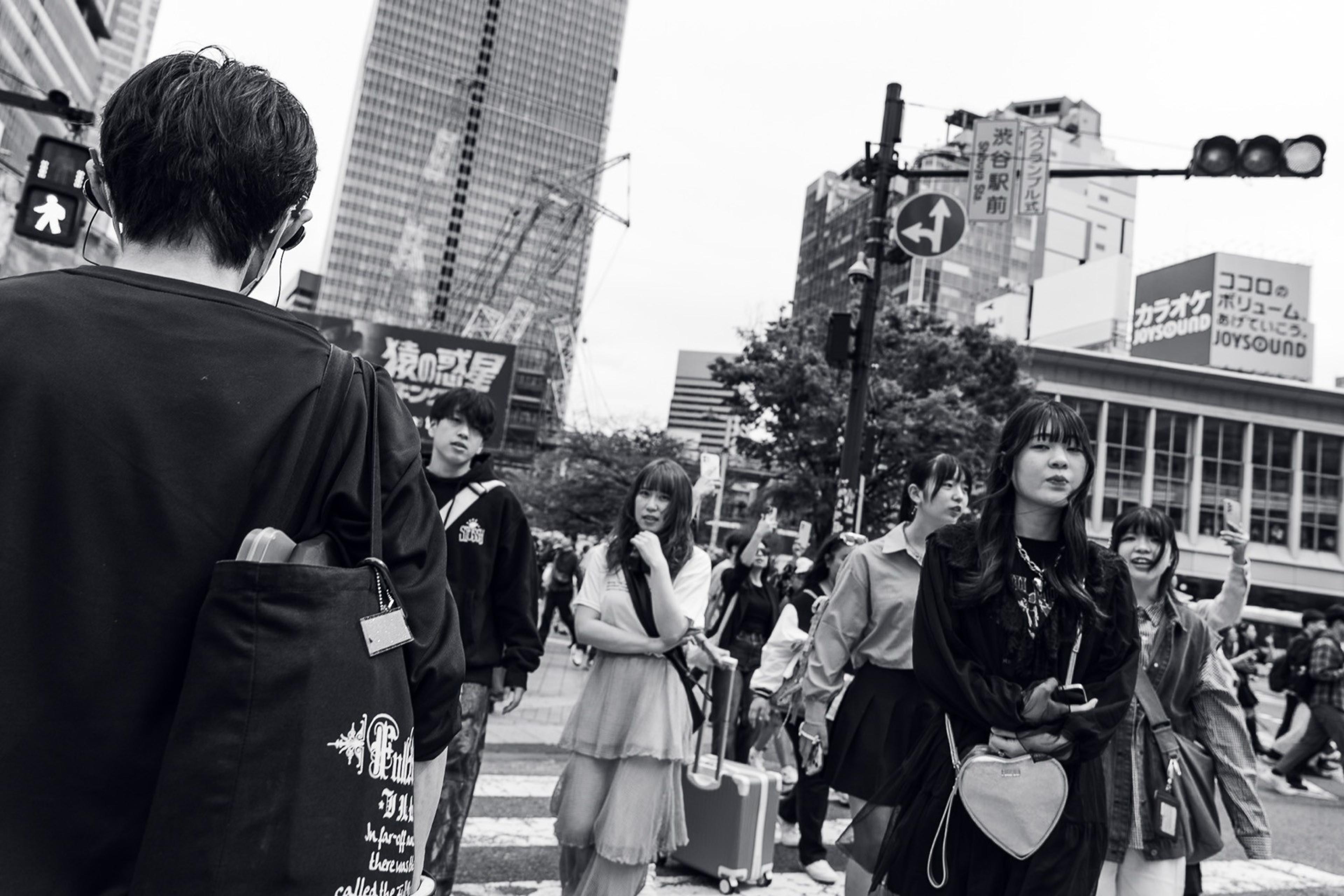 Black and white shot of young people crossing a crowded city intersection under traffic lights