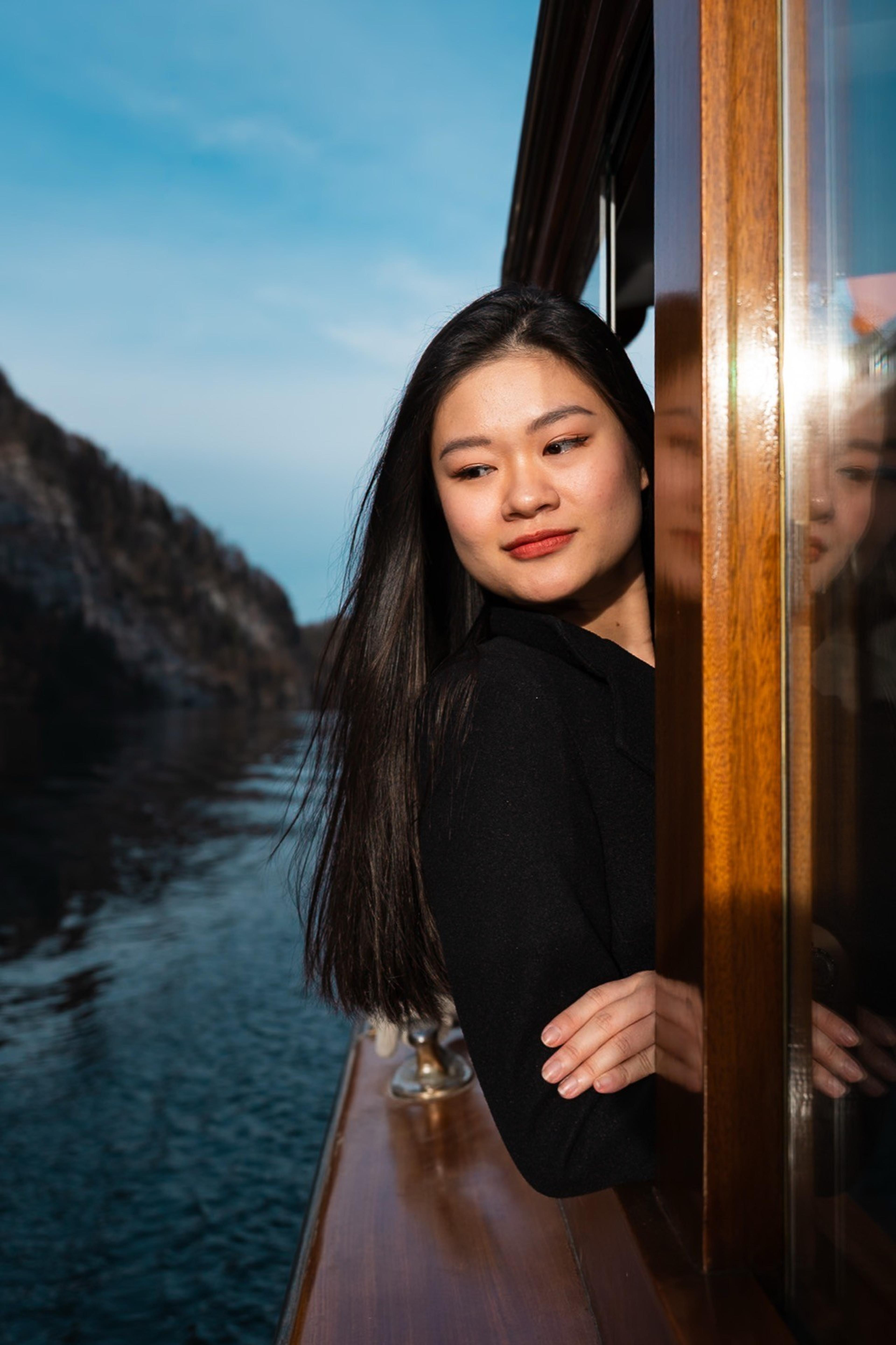 Woman leaning out of a wooden boat window on a calm river between dark rocky cliffs