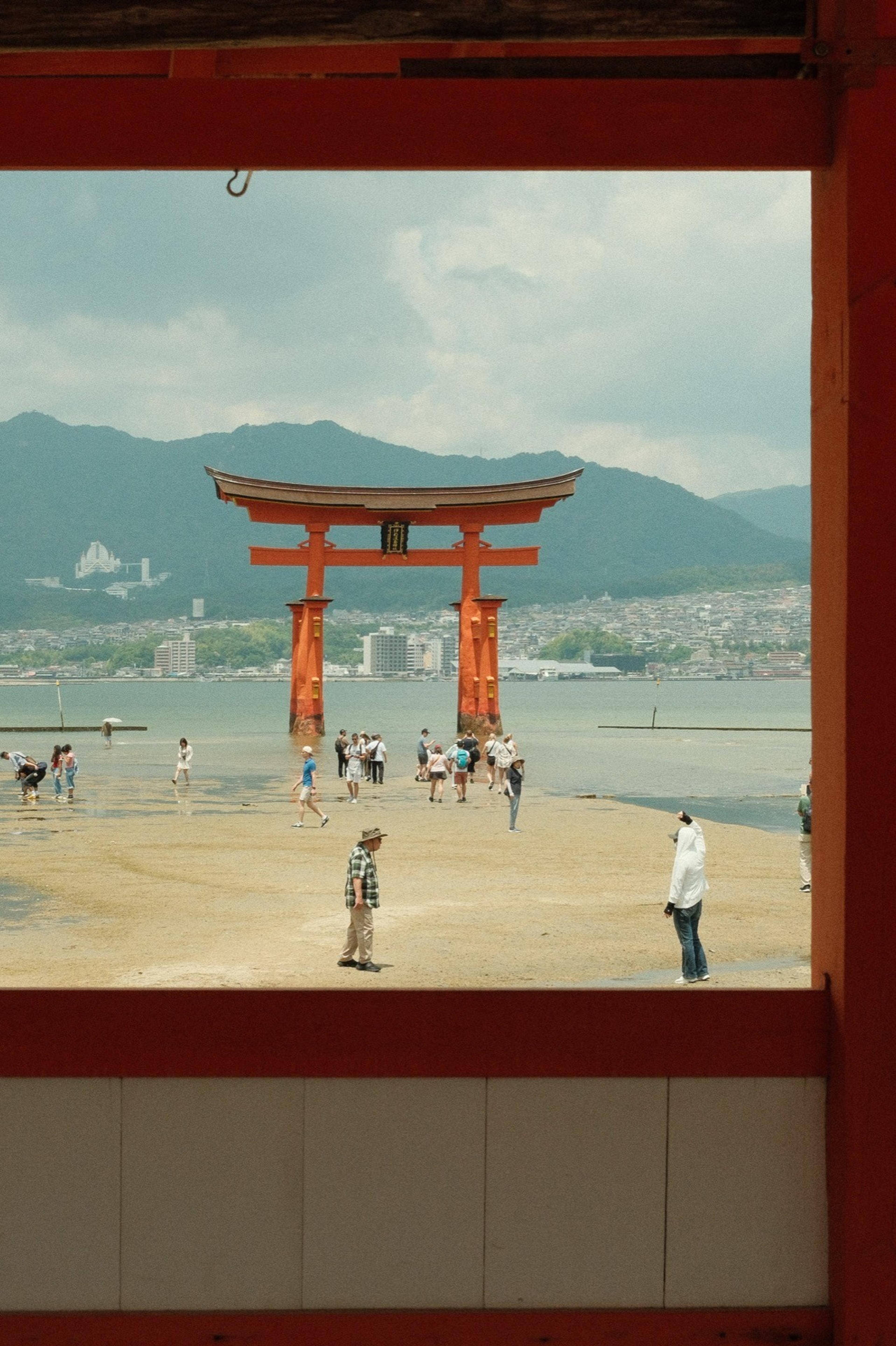 Large red torii gate in the shallows at low tide, seen through a red wooden window frame