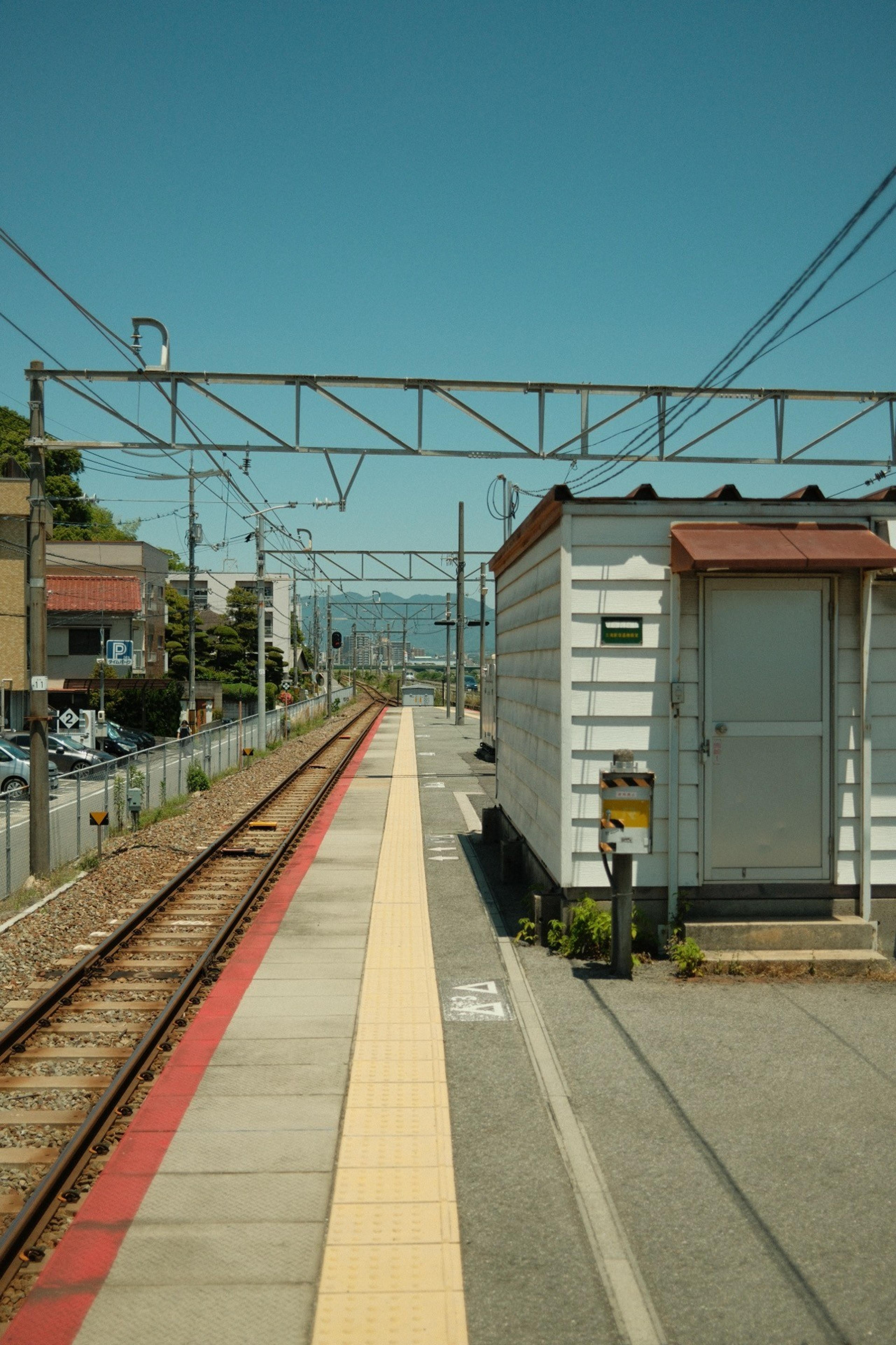 Empty train platform with a yellow tactile strip running alongside the tracks under a blue sky