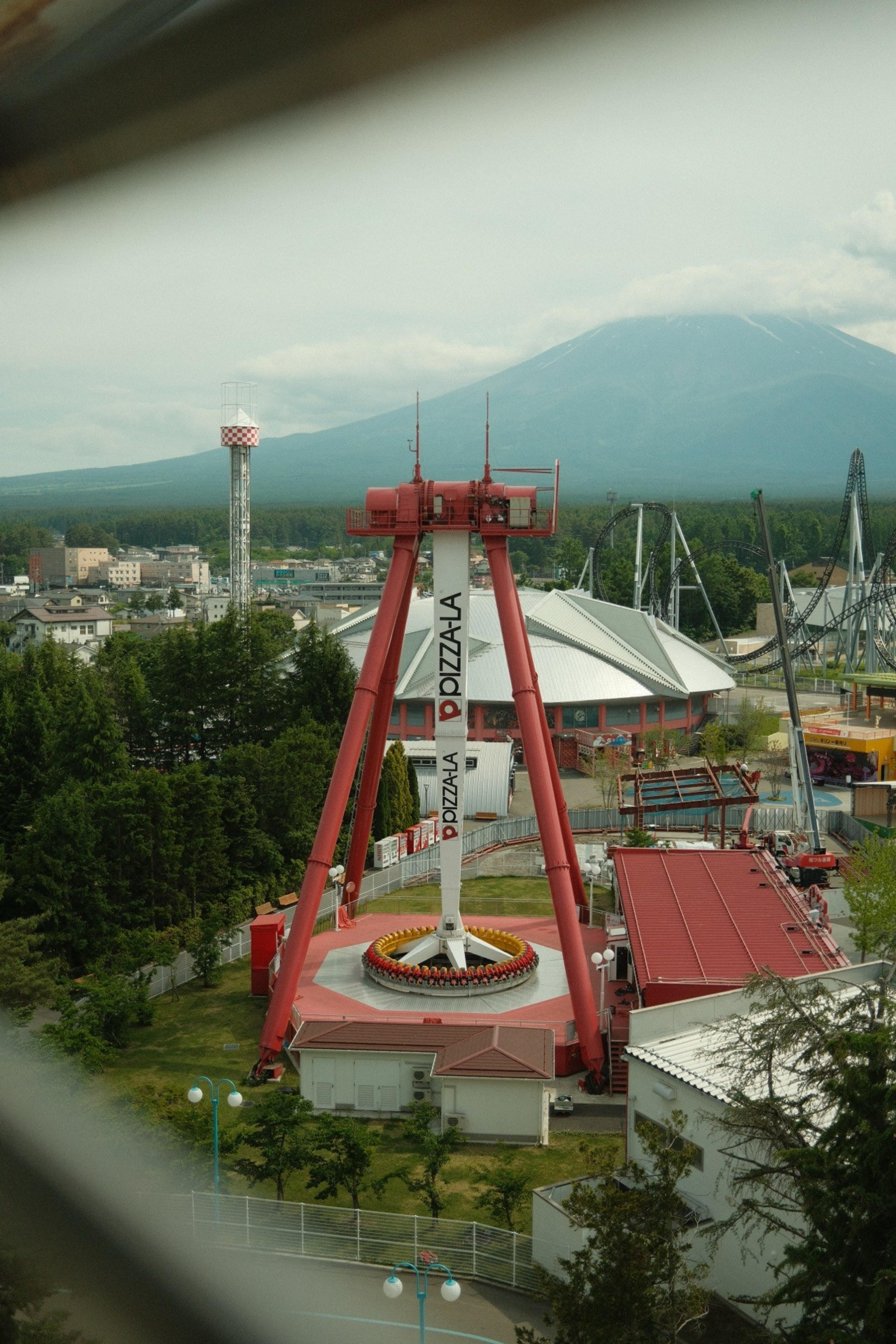 Red drop-tower ride at an amusement park with a large mountain rising behind under clouds