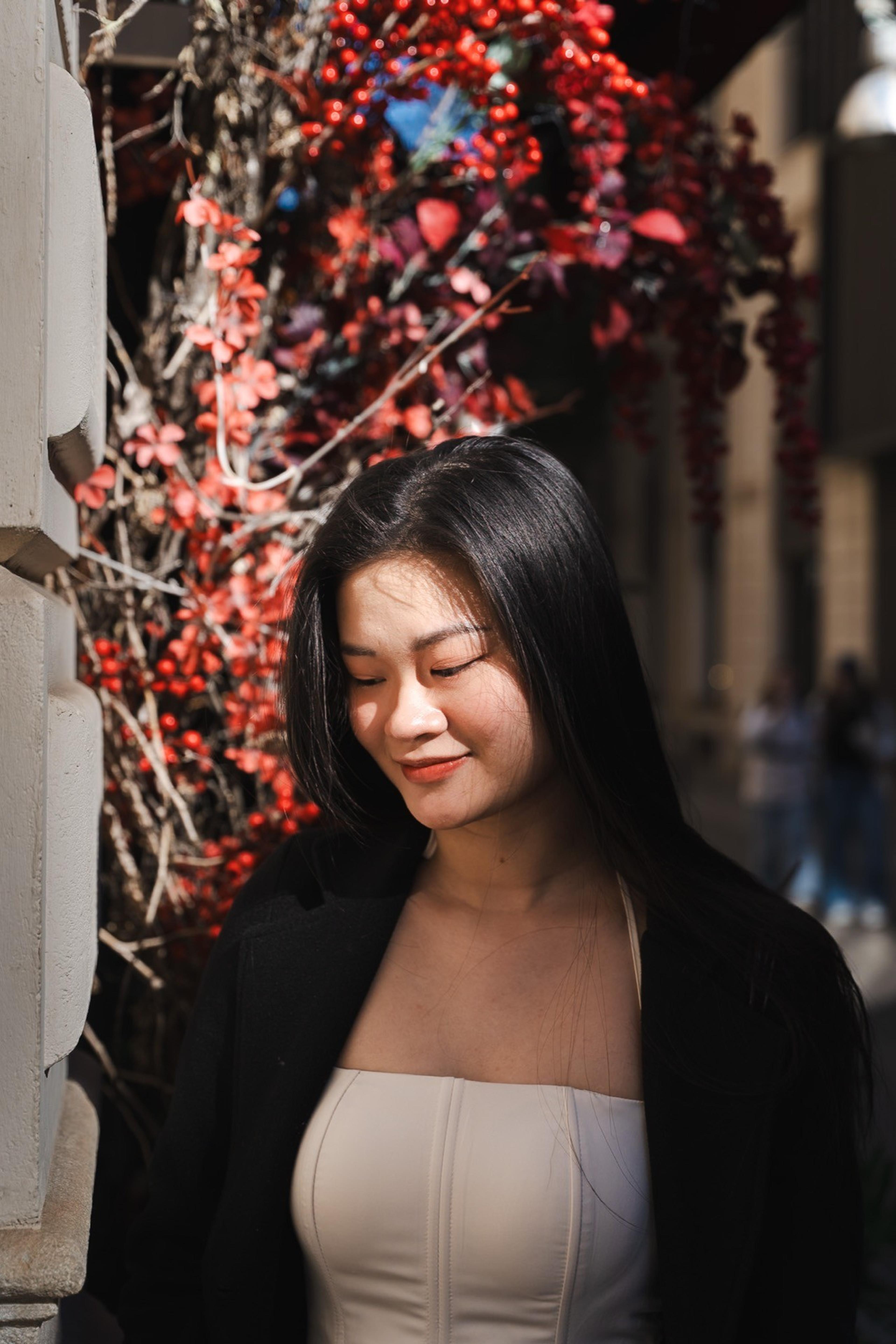 Woman in a black jacket smiling downward beside a wall of red autumn vines