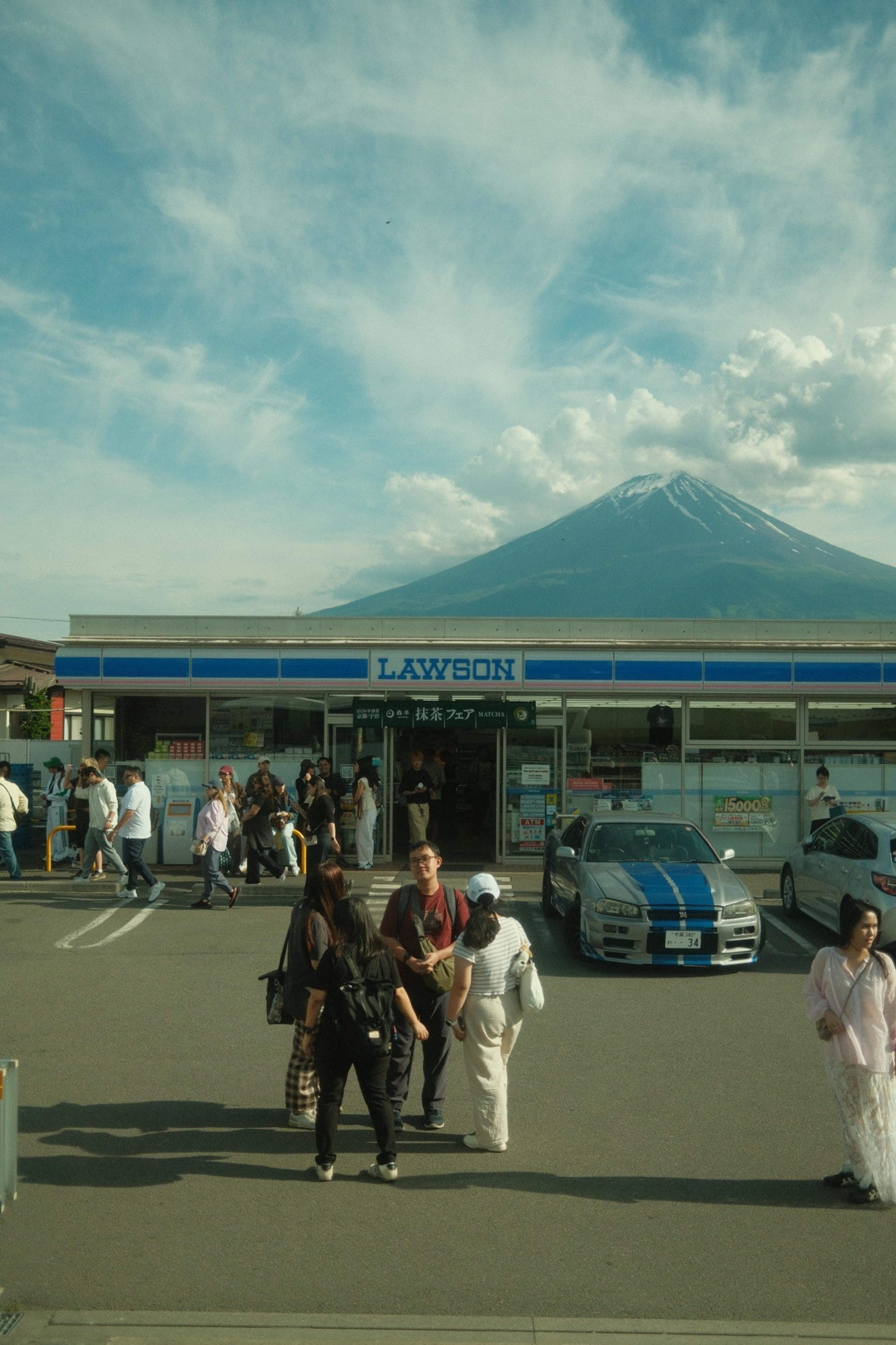 Tourists outside a Lawson convenience store with a snow-capped mountain rising above the roof