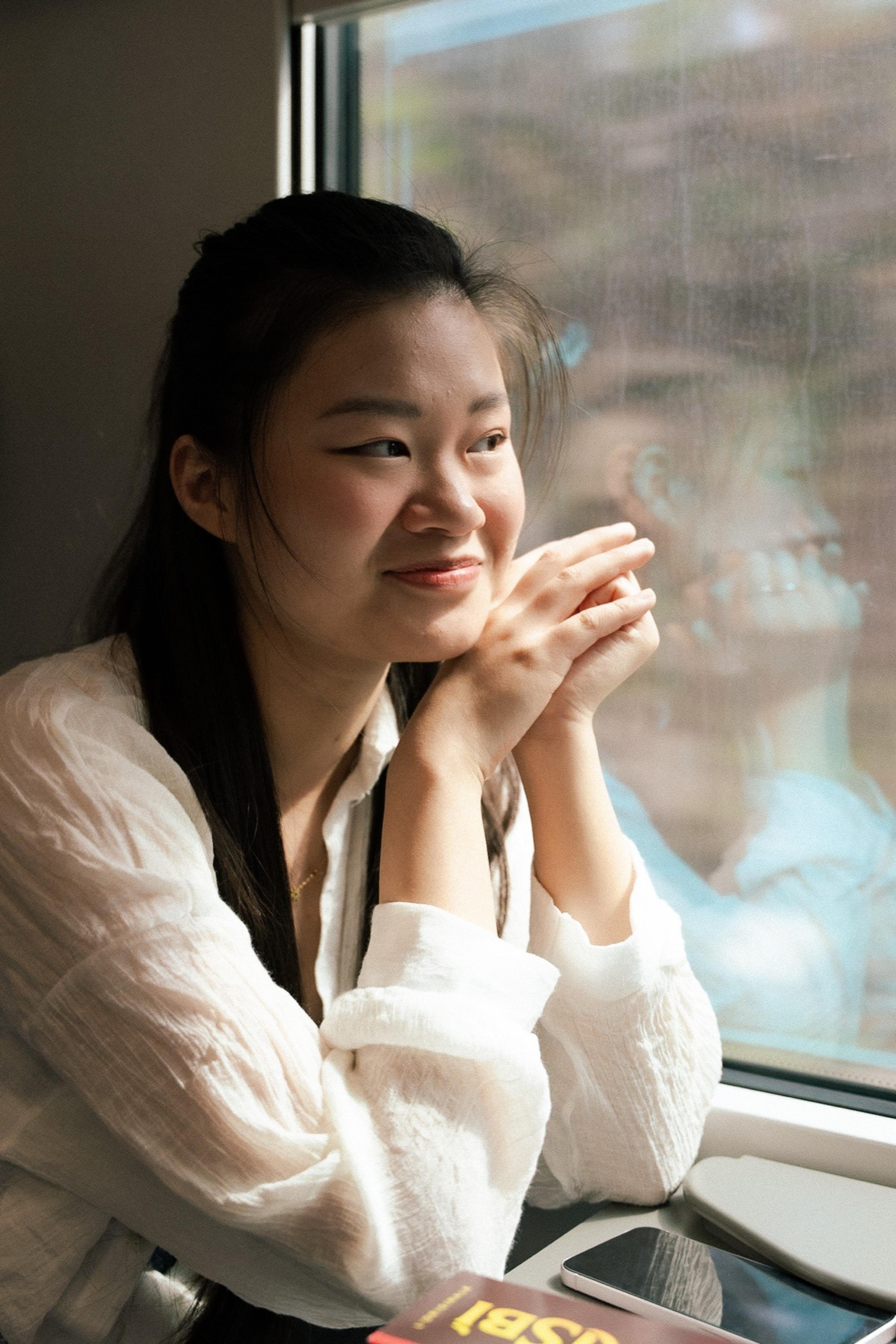 Smiling woman in a white shirt resting her chin on her hands by a train window
