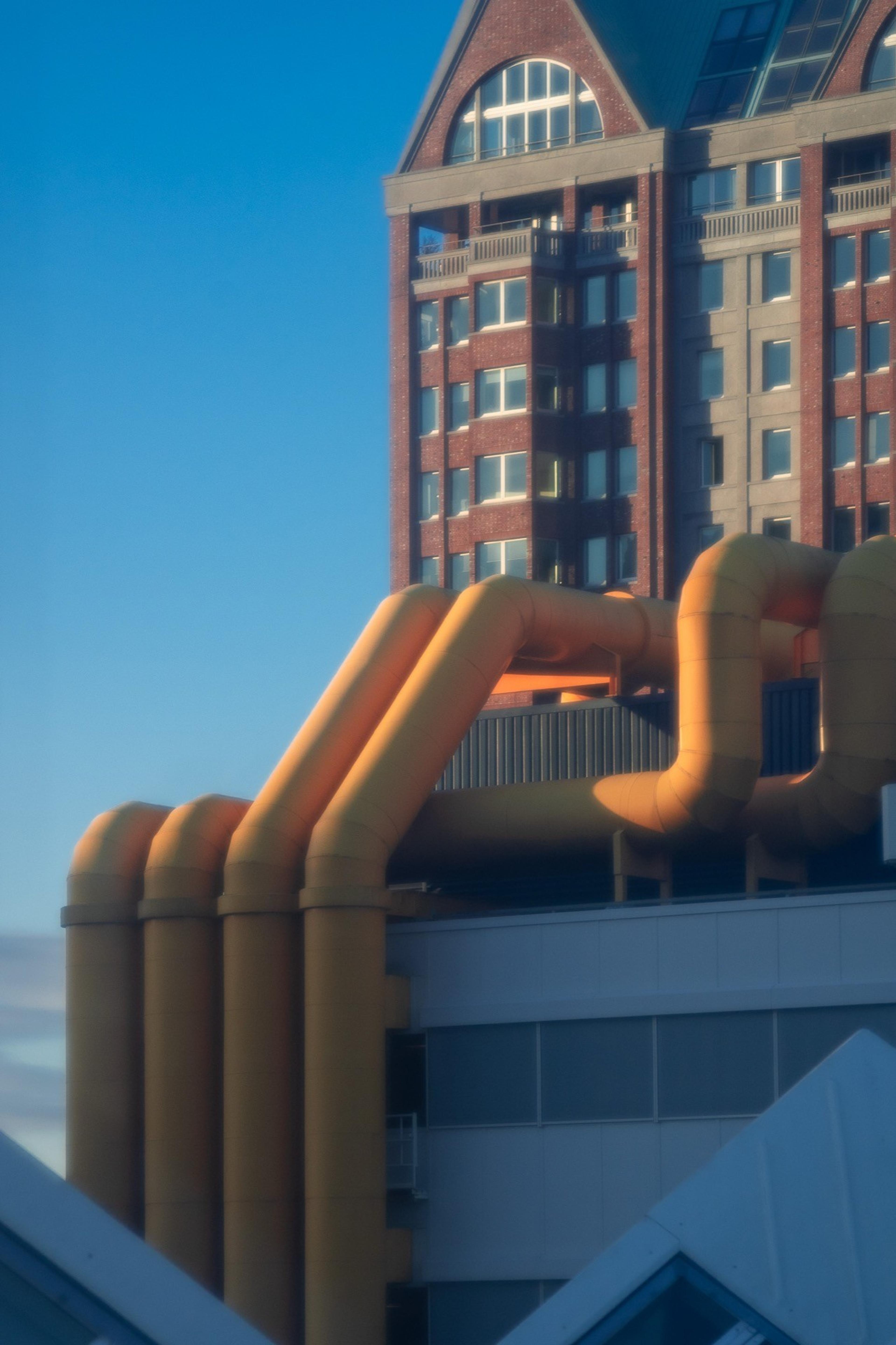 Oversized orange pipes snaking across a rooftop below a brick tower in golden evening light