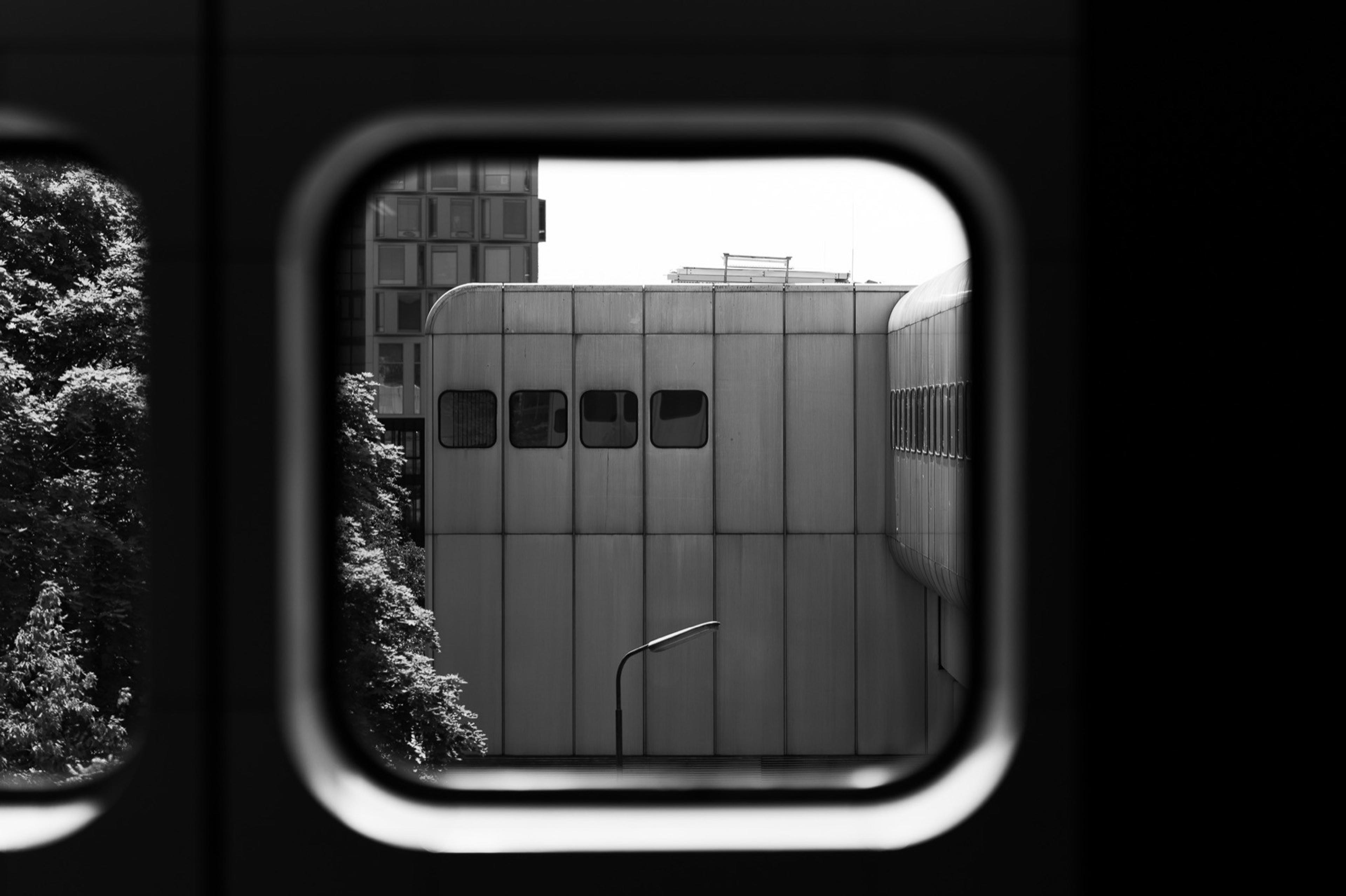 Black and white view through a rounded train window of a concrete building with small windows