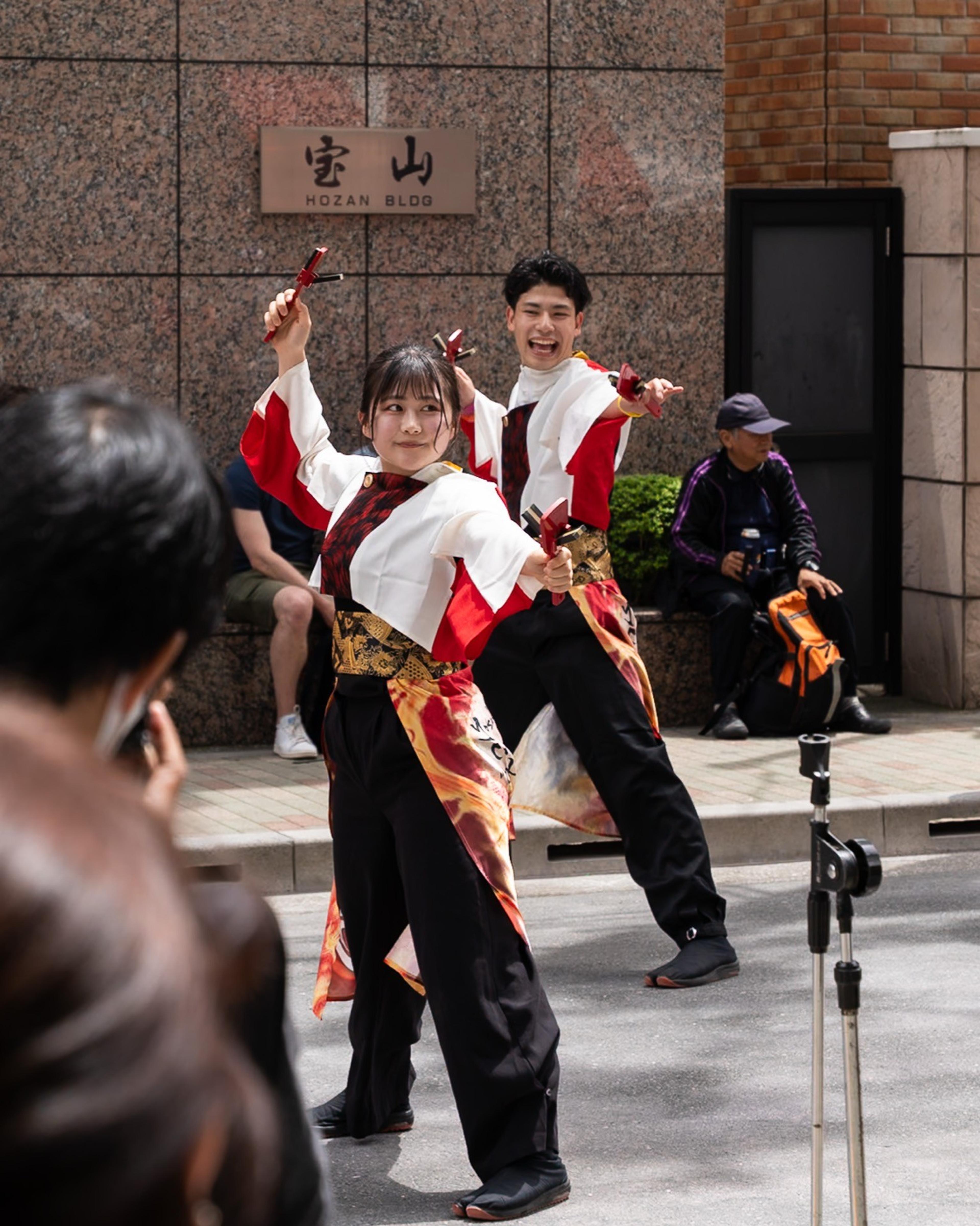 Two dancers in red, white and gold costumes performing with clappers at a street festival