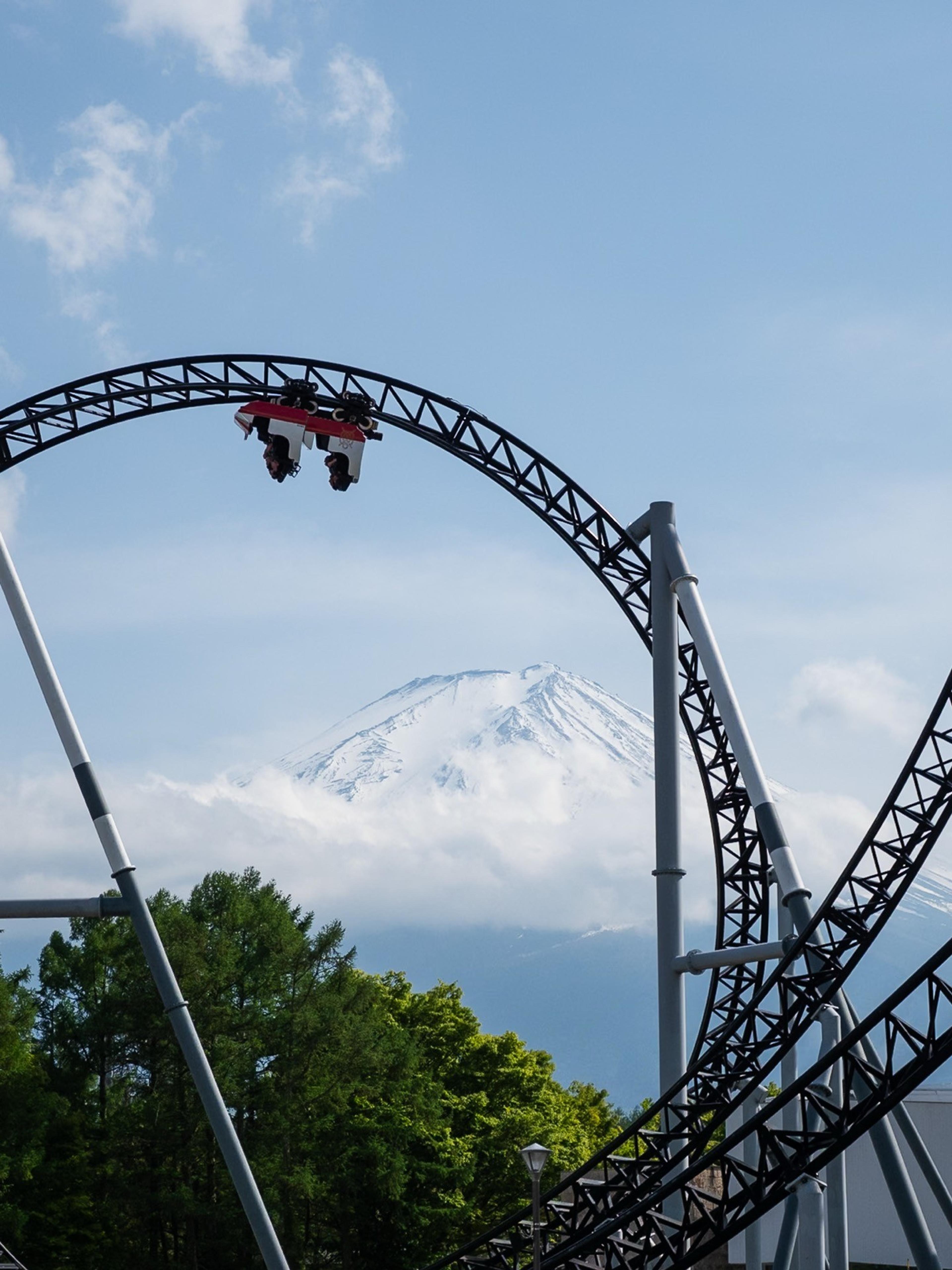 Roller coaster car hanging upside down on a loop with a snow-capped mountain in the distance