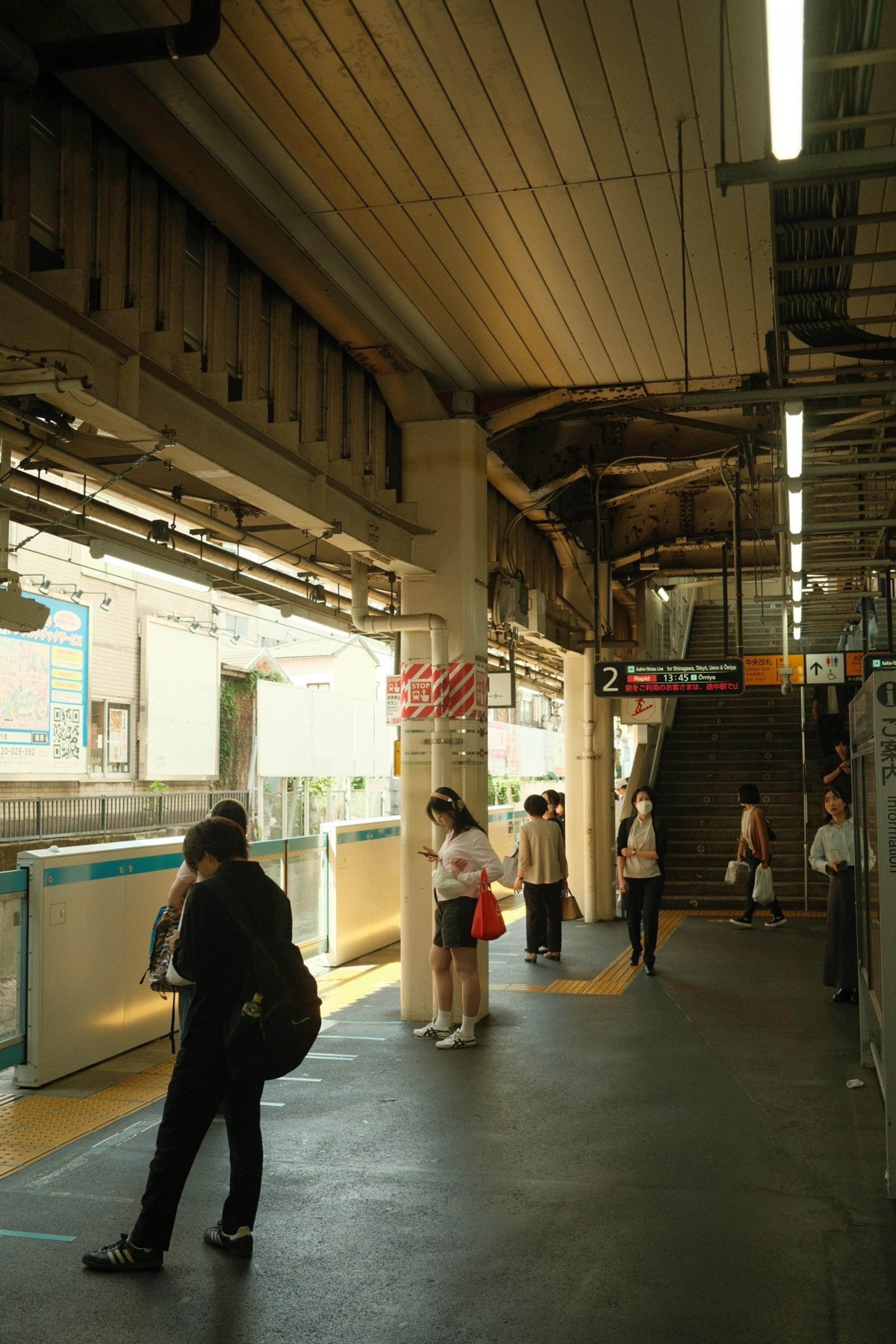 Commuters waiting on a covered train platform with Japanese signage in warm afternoon light