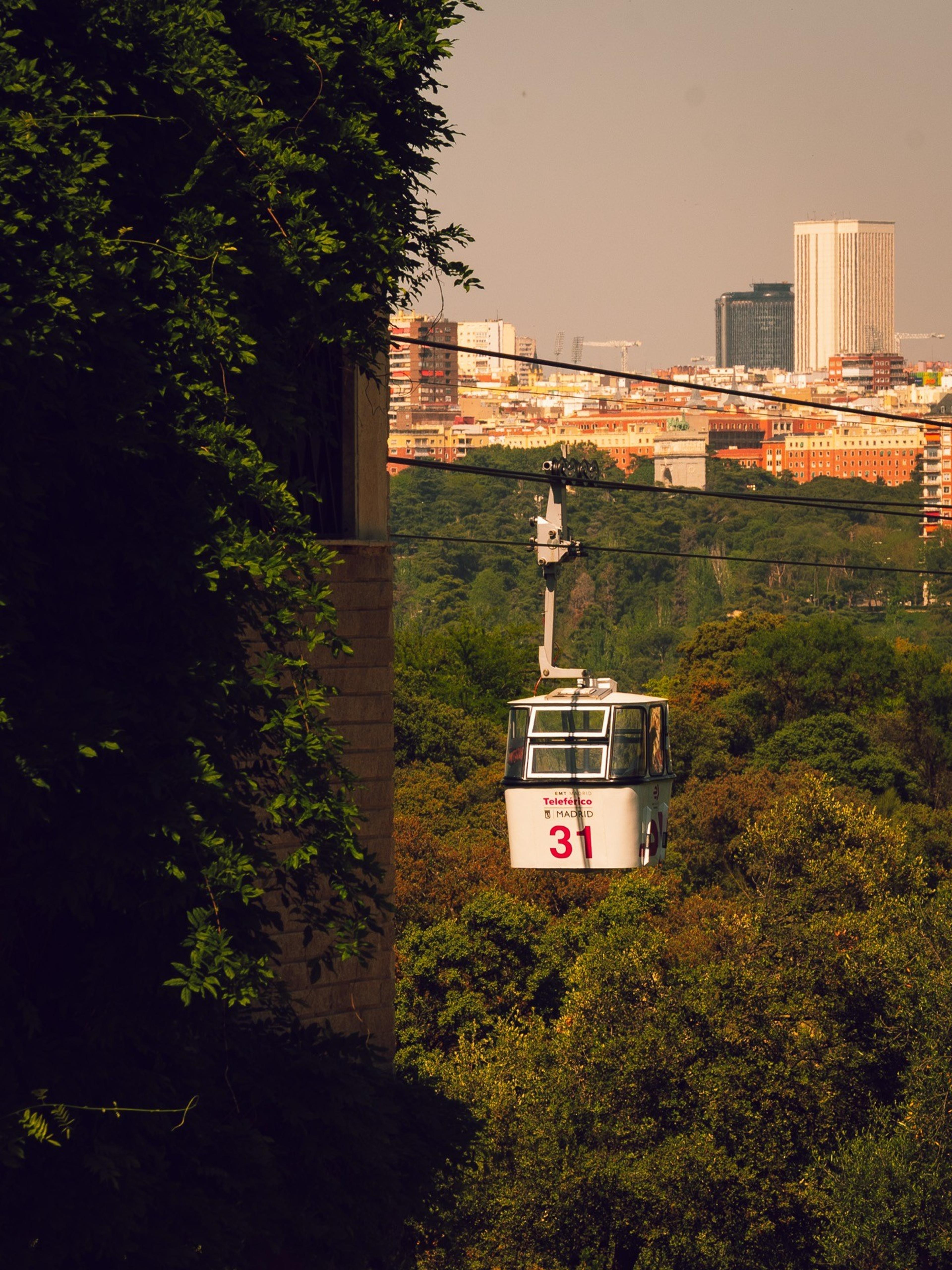 Teleférico Madrid cable car number 31 gliding over a wooded park toward the city skyline