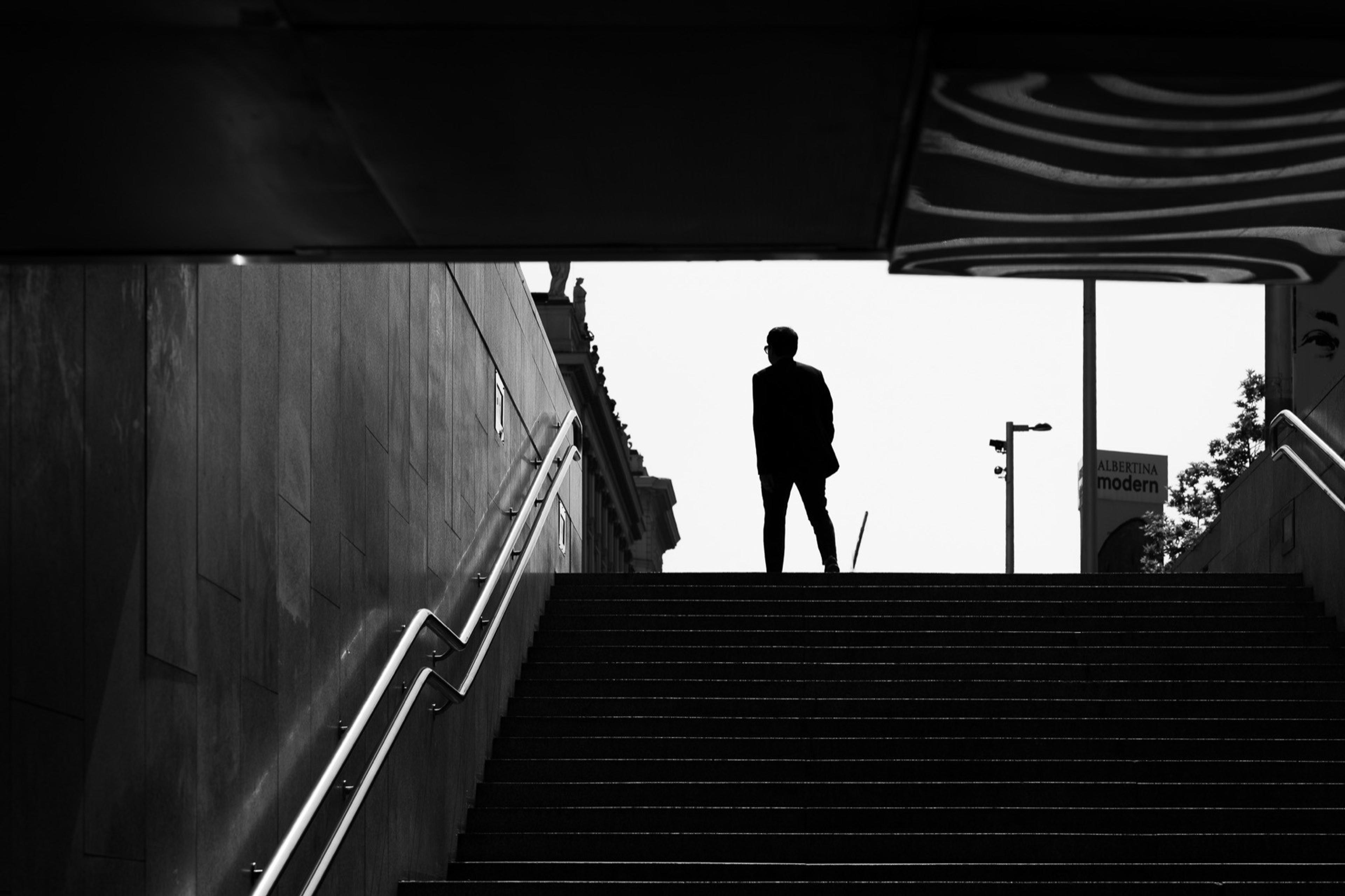 Black and white silhouette of a man at the top of a staircase leading out of an underpass