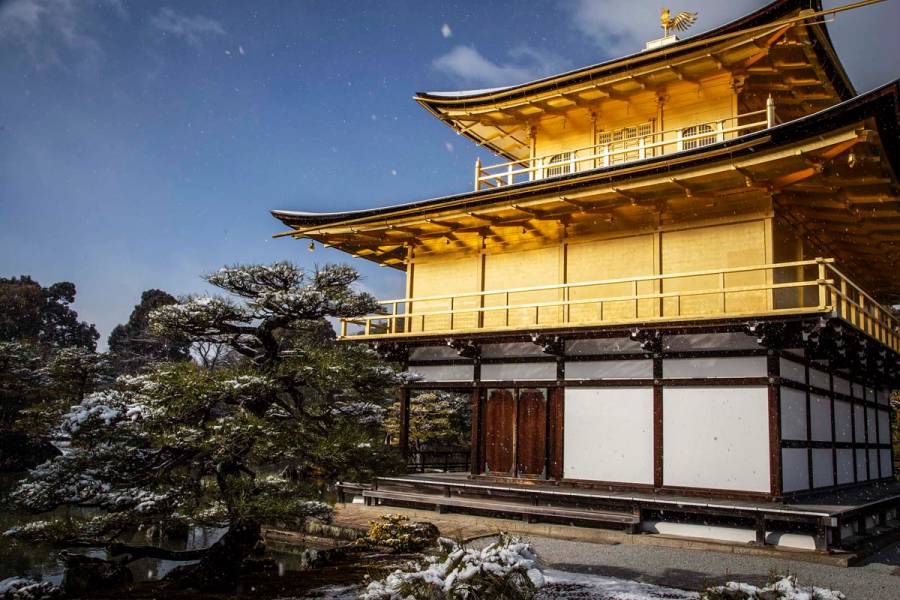 Kinkaku-ji, the Golden Pavilion in Kyoto, with snow falling on the pine garden and pond on a winter morning.