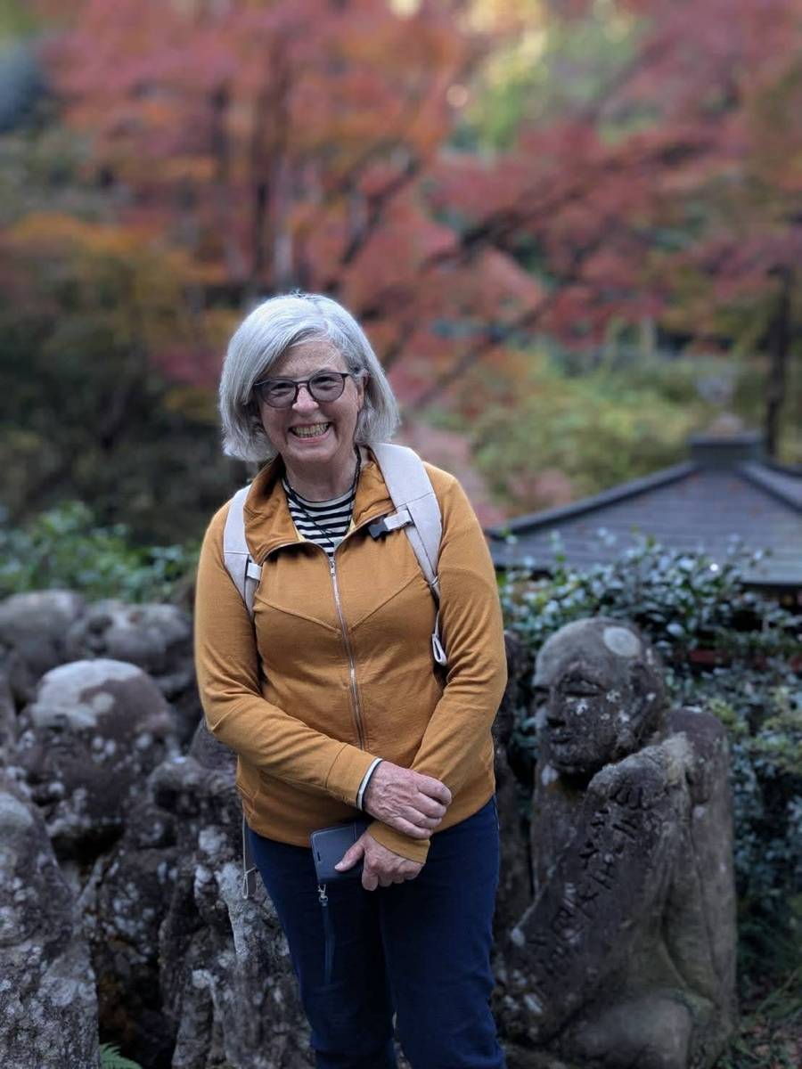Senior woman smiling at Kyoto temple garden with stone Jizo statues and autumn foliage during bike tour