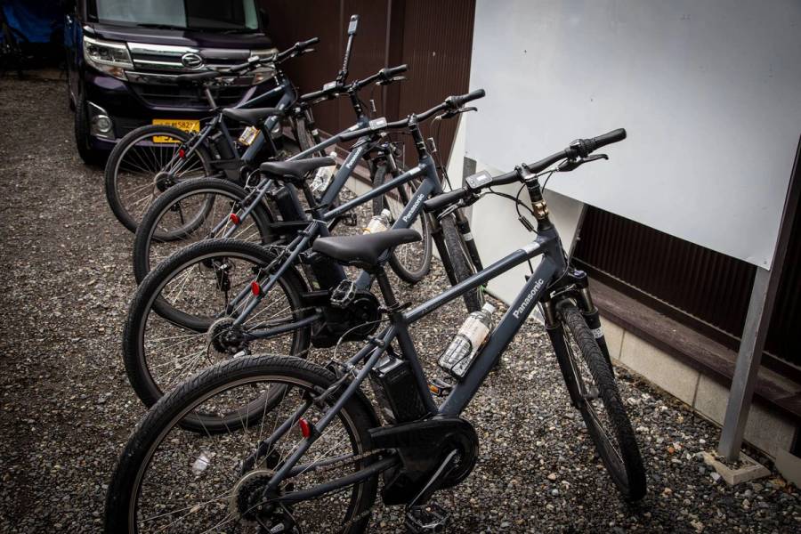 A row of Panasonic e-bikes parked on gravel at NORU Kyoto Bike Tours, showing the mid-drive motor and battery unit on the frame.