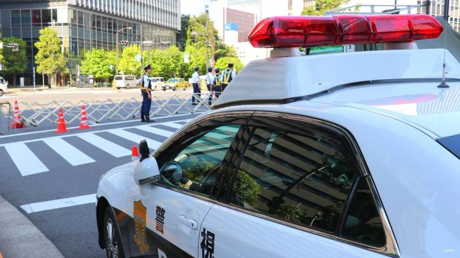 Japanese police car in the foreground with uniformed officers managing a city intersection, Tokyo, Japan.