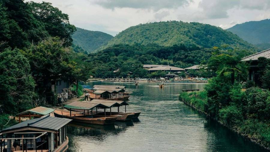 Traditional wooden rental boats moored on the Oi River in Arashiyama, Kyoto, with densely forested green mountains in the background in summer