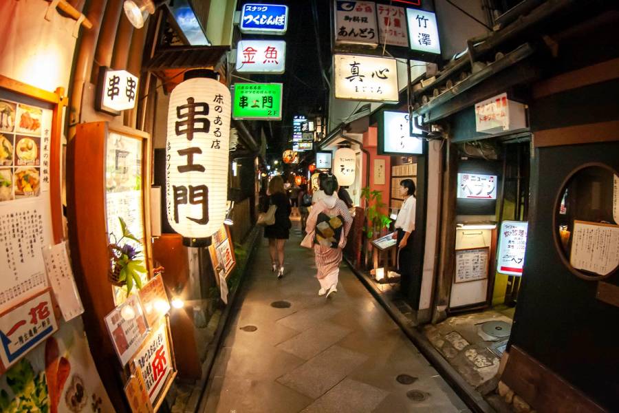 Pontocho alley in Kyoto at night, with paper lanterns, glowing signs, and two women walking, one in a yukata.