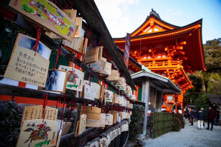 Wooden ema prayer plaques hang in rows at Kamigamo Shrine in northern Kyoto, with the vermillion tower gate rising in the background against a clear winter sky.
