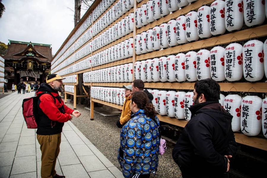 Tour guide explaining cultural significance of traditional Japanese lanterns to small group at Kyoto shrine
