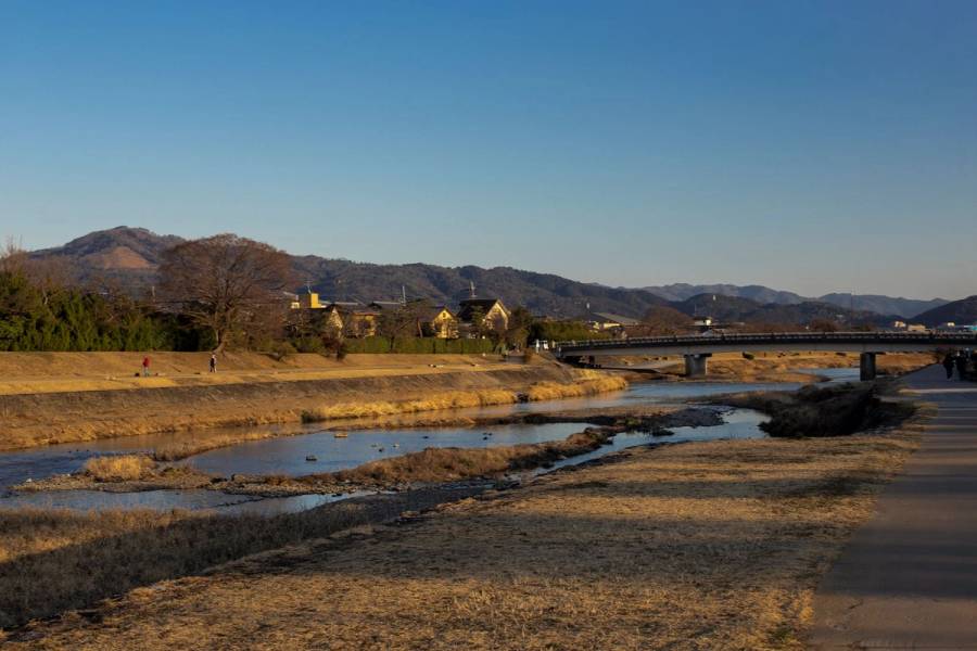 The Kamo River under a clear blue winter sky, dry grass along the banks and a bridge in the distance.