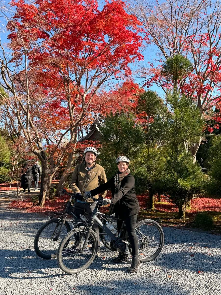 Two cyclists with e-bikes posing at Kyoto temple surrounded by vibrant red autumn maple trees