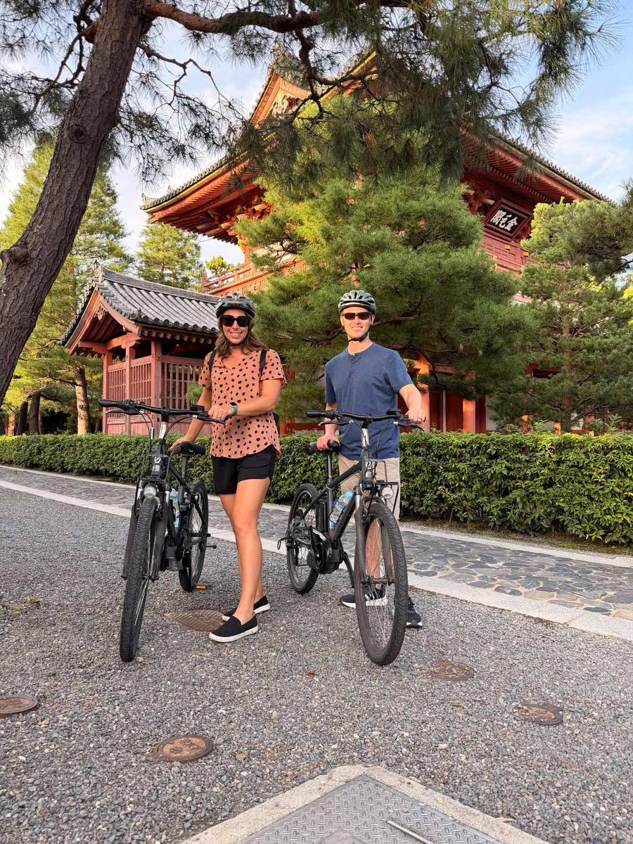 A couple with bicycles inside the grounds of Daitokuji Temple in Kyoto, Japan. They are standing in front of a temple located in the middle of the temple complex.