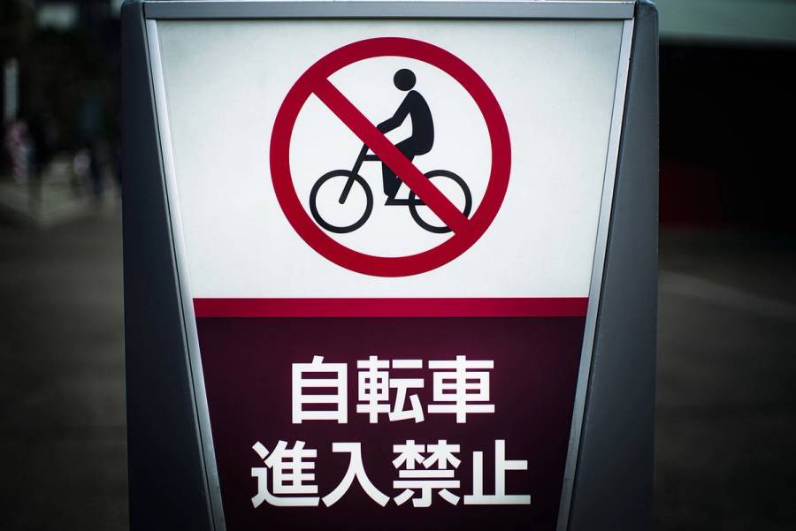 A Japanese no-cycling sign reading 自転車進入禁止 (bicycle entry prohibited), mounted on a post on a street in Japan.