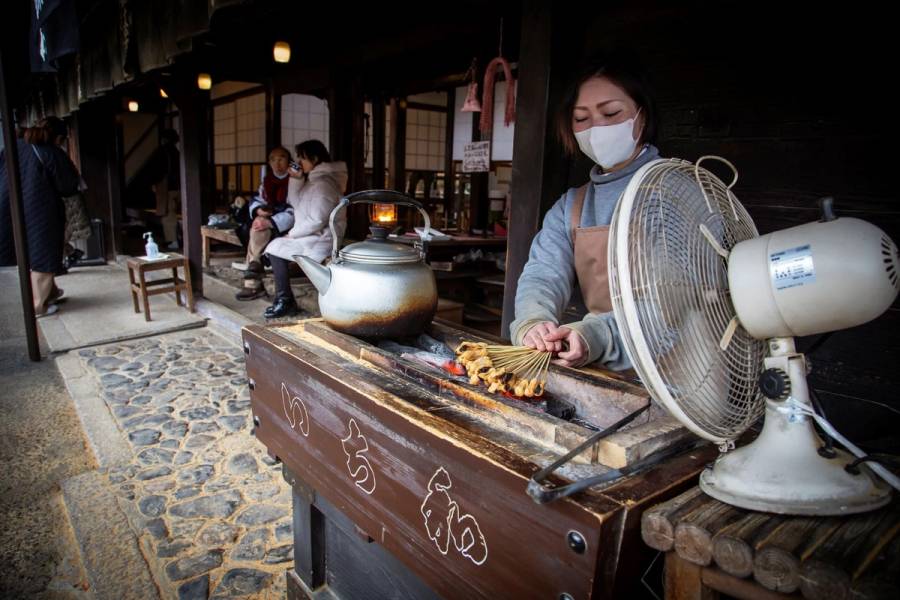 Woman grilling fresh mochi rice cakes over charcoal at traditional Japanese tea house during Kyoto bike tour stop