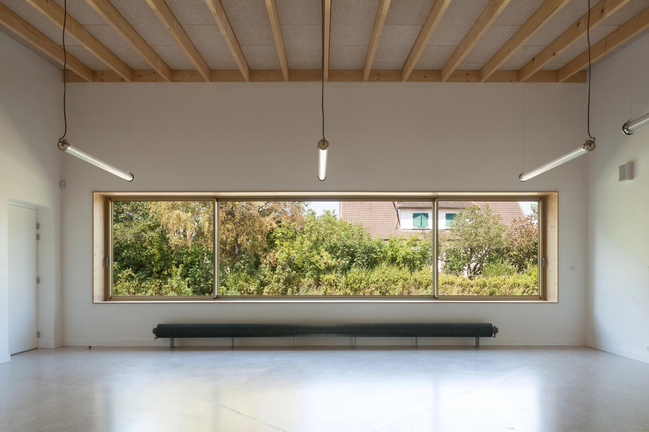 Intérieur de l’école élémentaire Hubert Reeves à Champagnole : salle lumineuse avec ossature bois apparente, grande baie vitrée sur le paysage arboré.