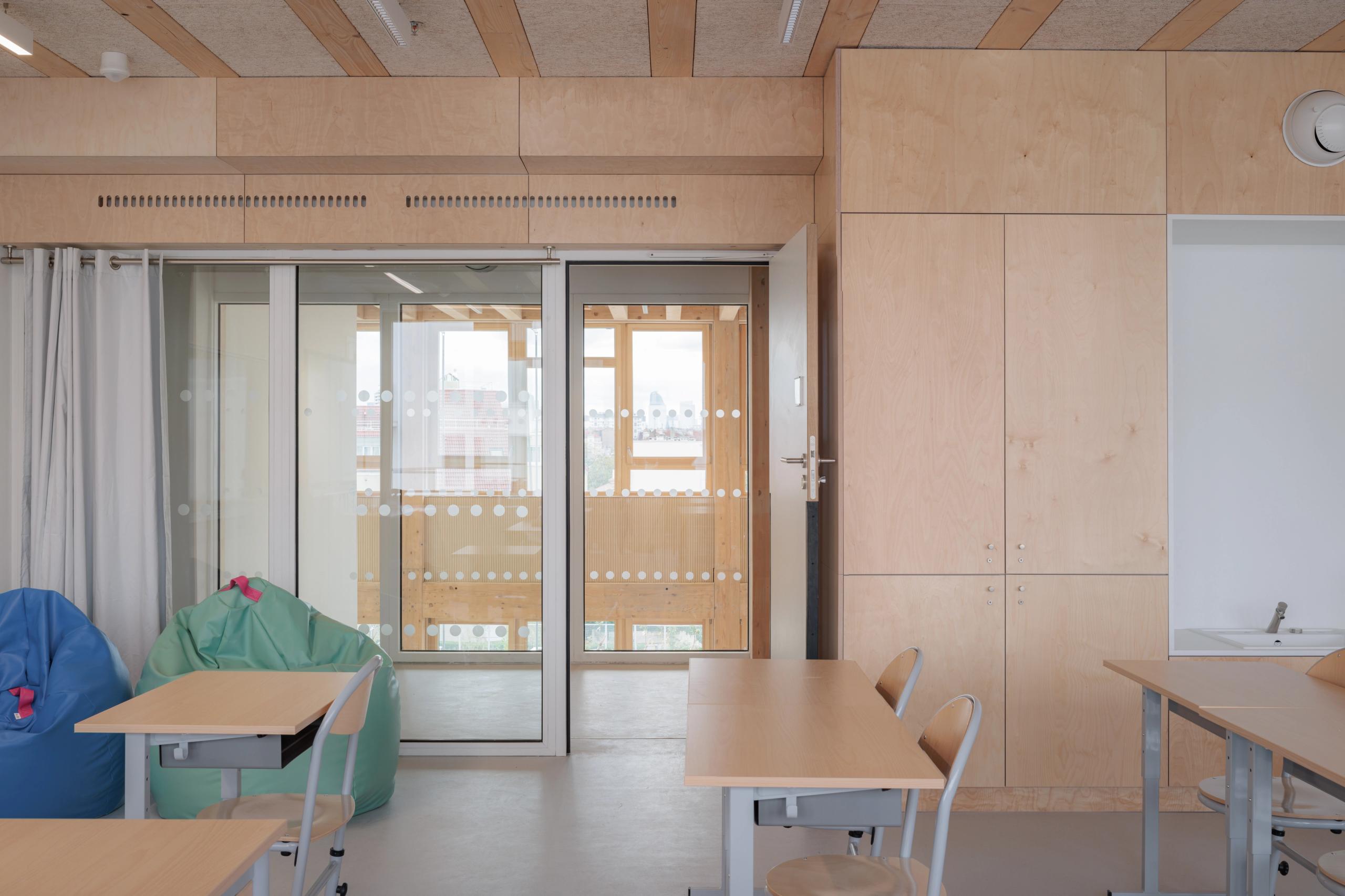 Salle de classe du groupe scolaire Dominique Frelaut à Colombes, menuiseries bois, cloisons vitrées sur loggia et mobilier épuré favorisant la lumière naturelle.