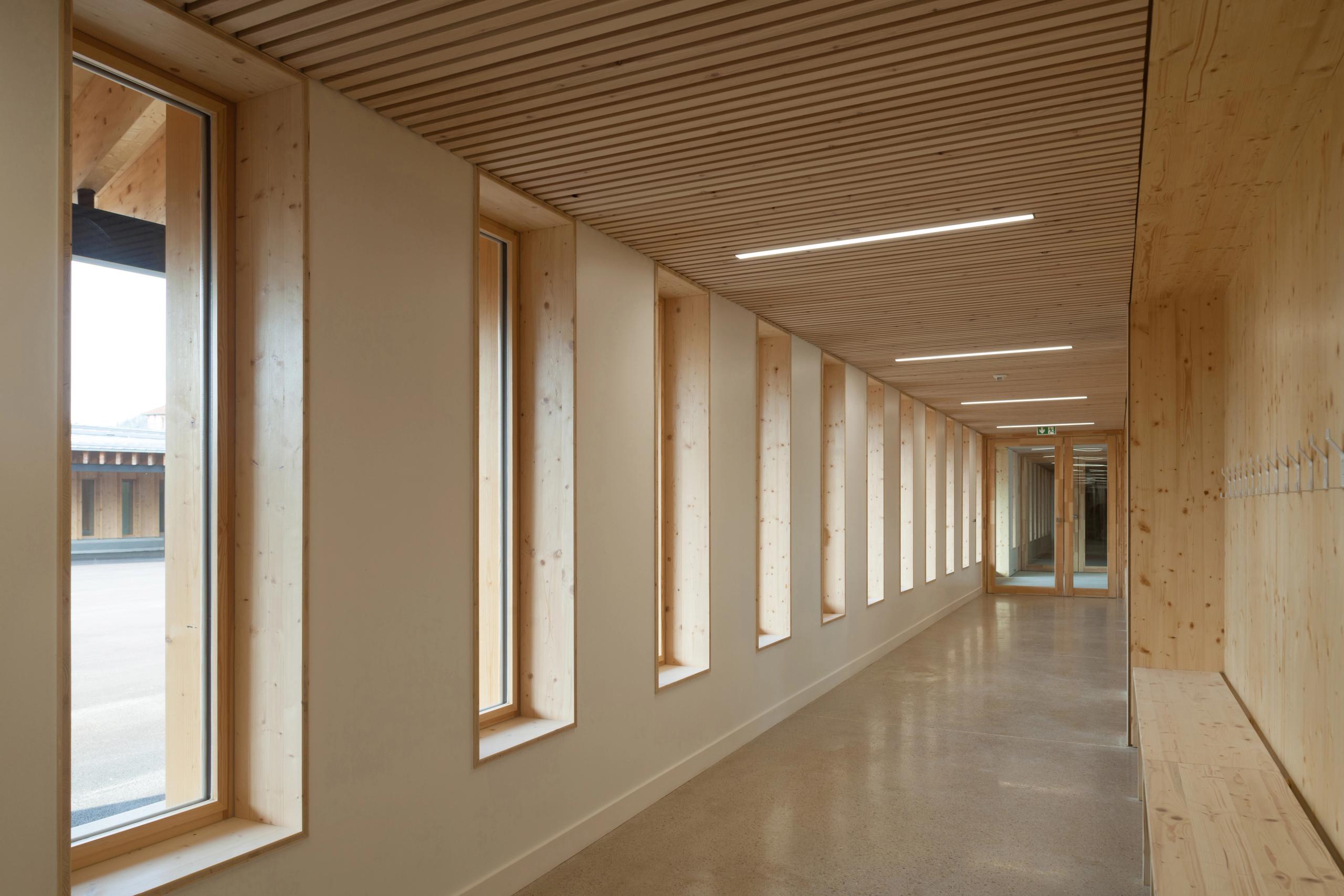Couloir de l’école élémentaire Hubert Reeves à Champagnole, ossature bois apparent, bandeau de fenêtres verticales et plafond à lames avec éclairage linéaire.