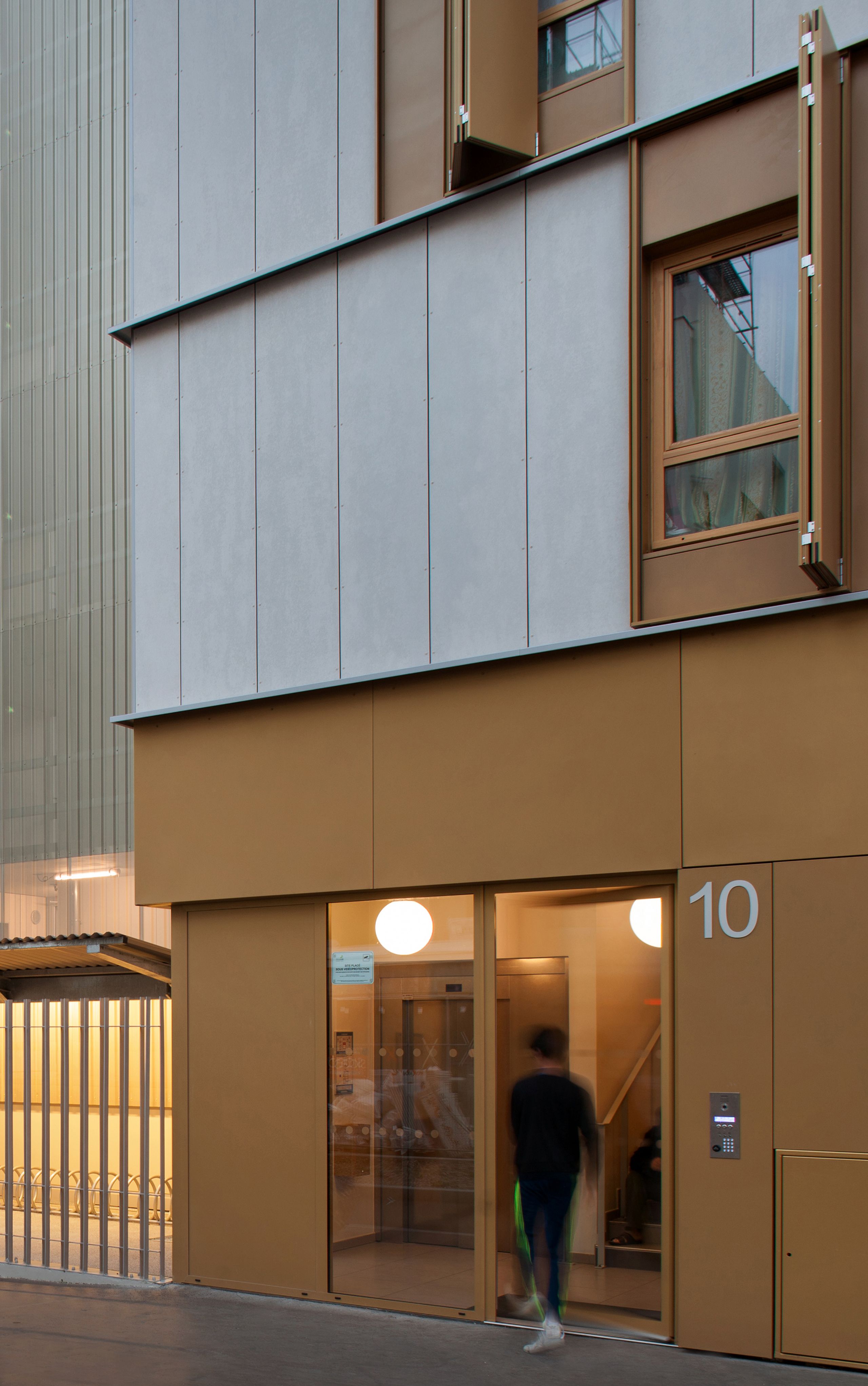 Façade des 55 logements à Lyon par Tectoniques, socle métallique ocre, parement béton clair, volets pliants, hall vitré numéroté 10 en rez-de-chaussée.