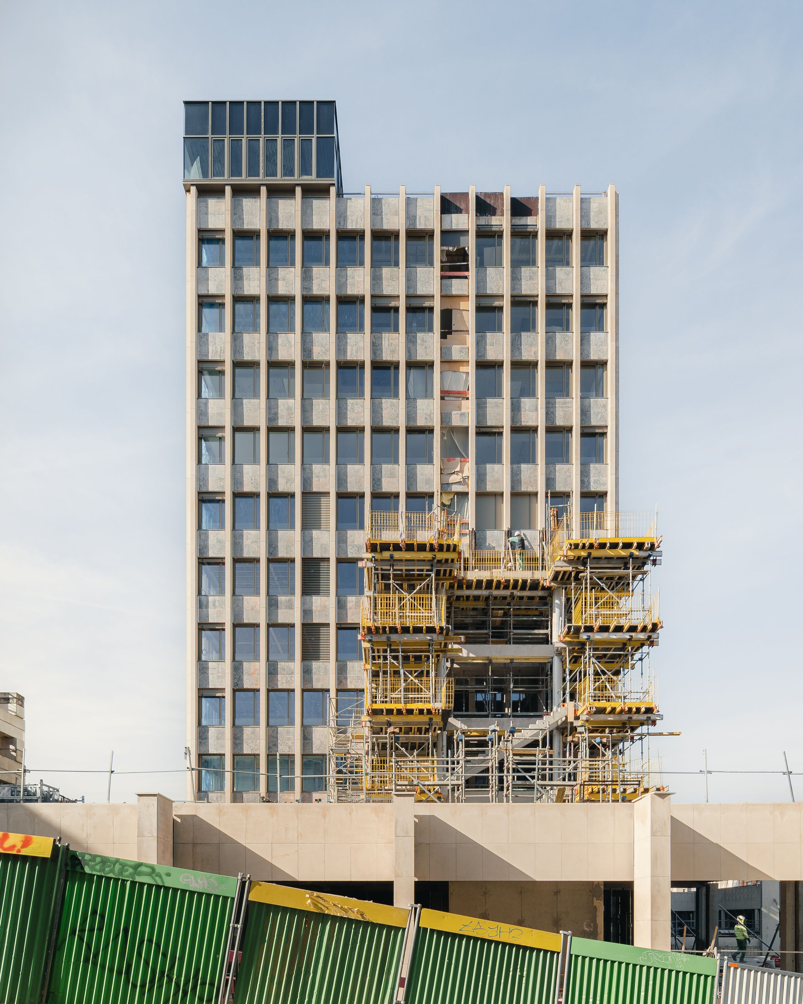 Chantier de réhabilitation de l’IGH Émile Loubet à Saint-Étienne, façade de tour moderniste en béton avec échafaudages centraux et attique vitré.