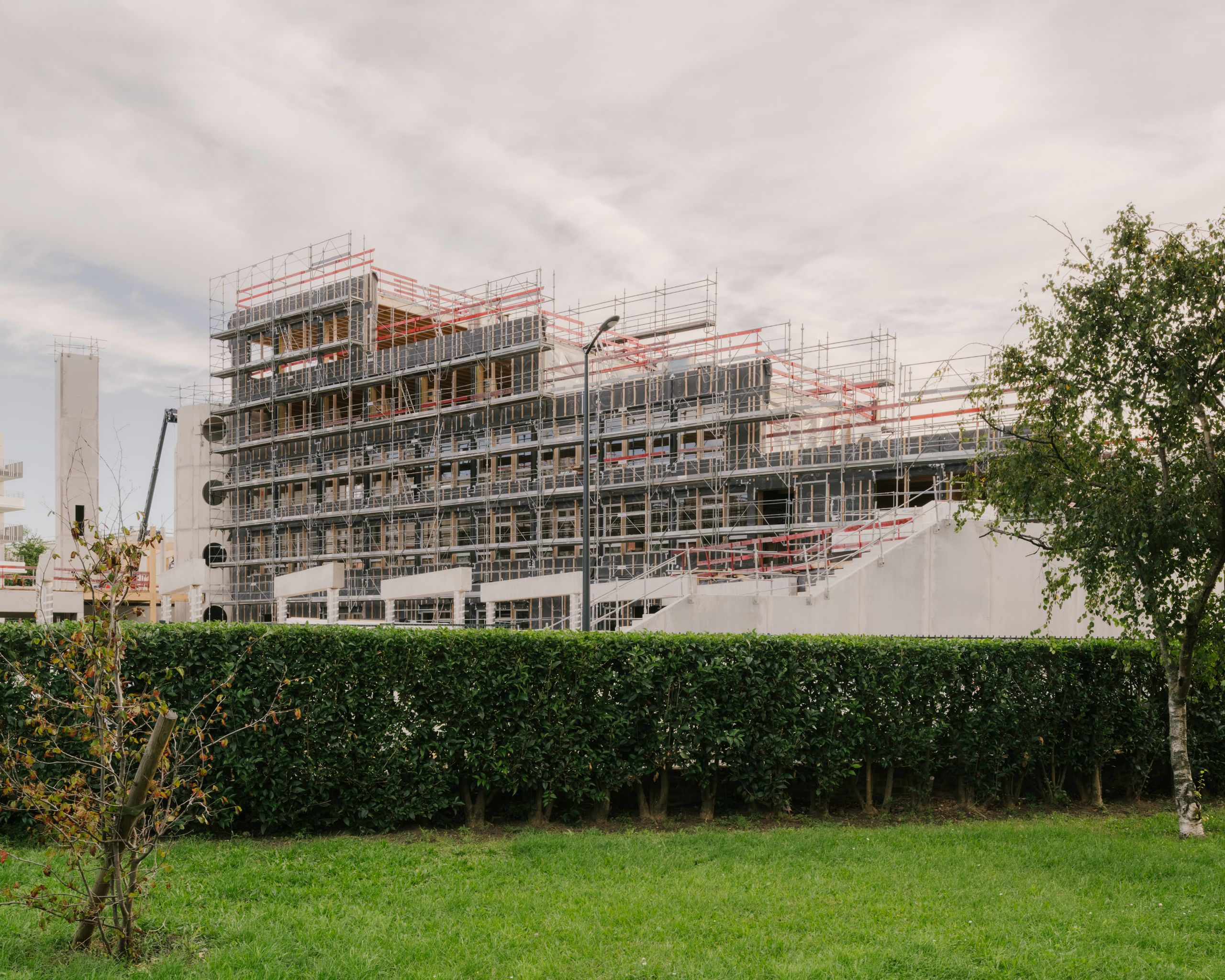 Chantier du groupe scolaire Dominique Frelaut à Colombes : volume en gradins en béton et métal, enveloppé d’échafaudages, dominant une cour plantée.