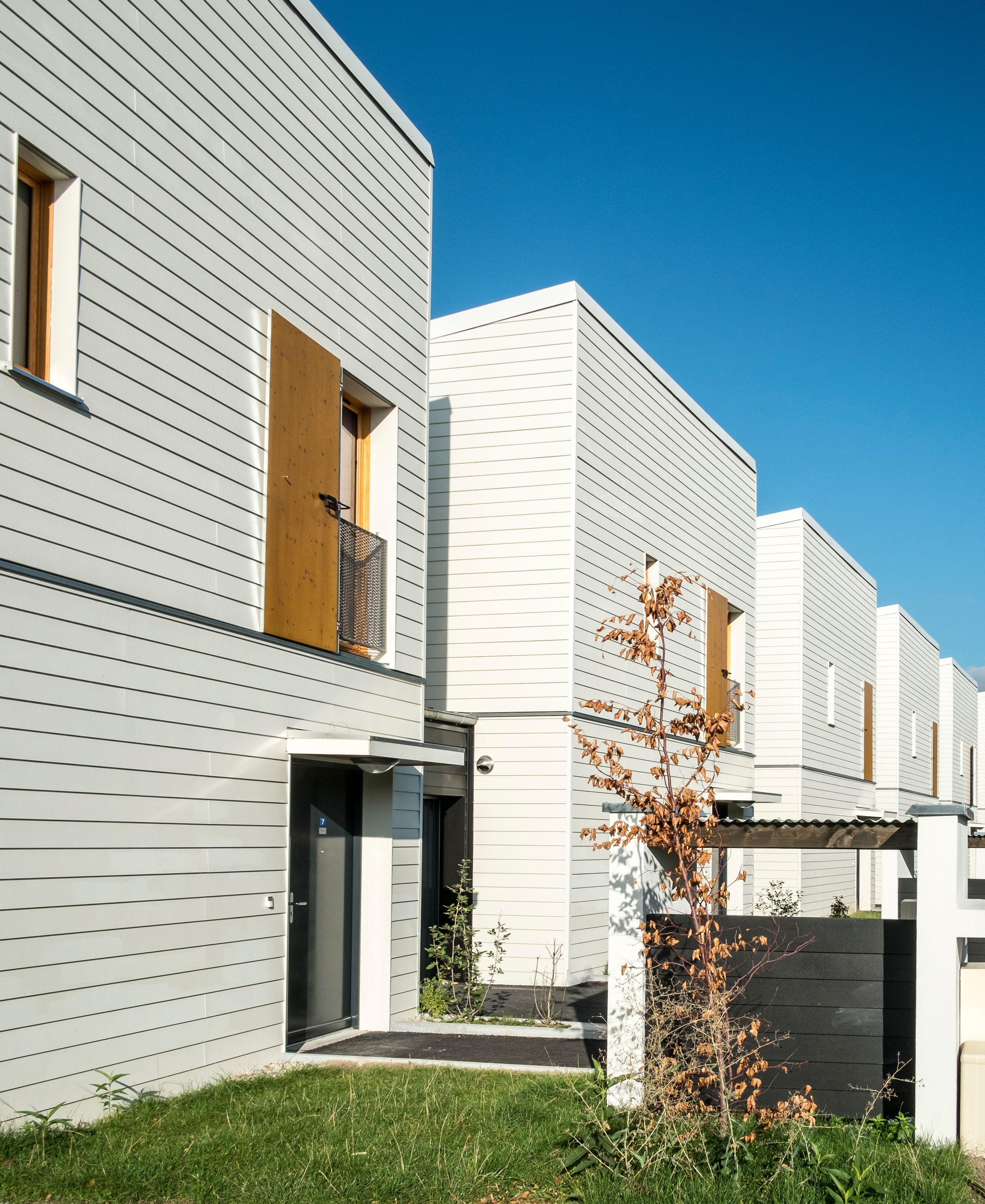 Façades en bardage horizontal clair des 60 logements Tectoniques à Rive-de-Gier, volumes compacts en bande, percements bois et cheminements extérieurs plantés.