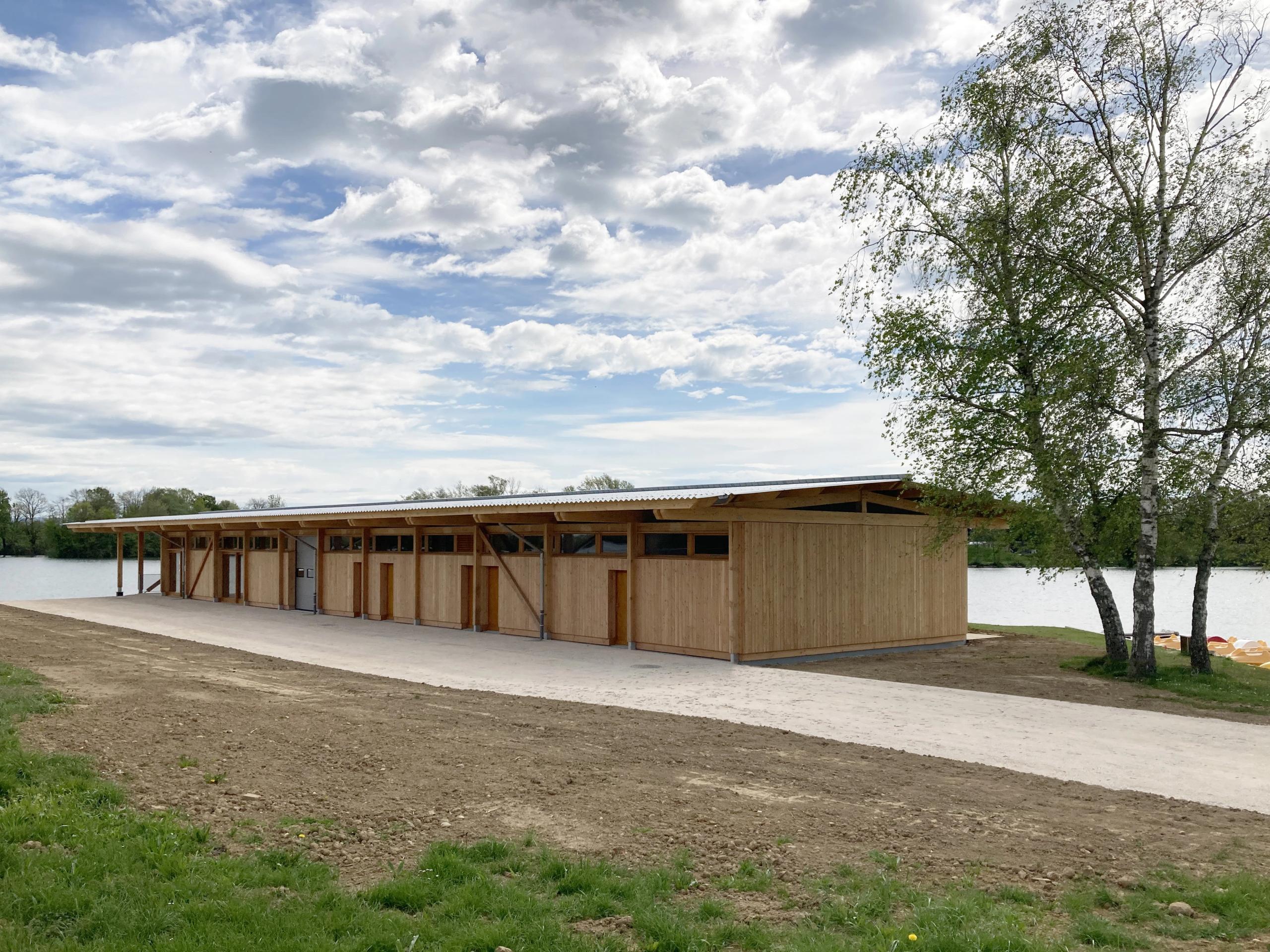 Maison des sports à Malafretaz : volume linéaire en ossature bois, bardage vertical, toiture légère débordante, ouvert sur le lac et le paysage arboré.