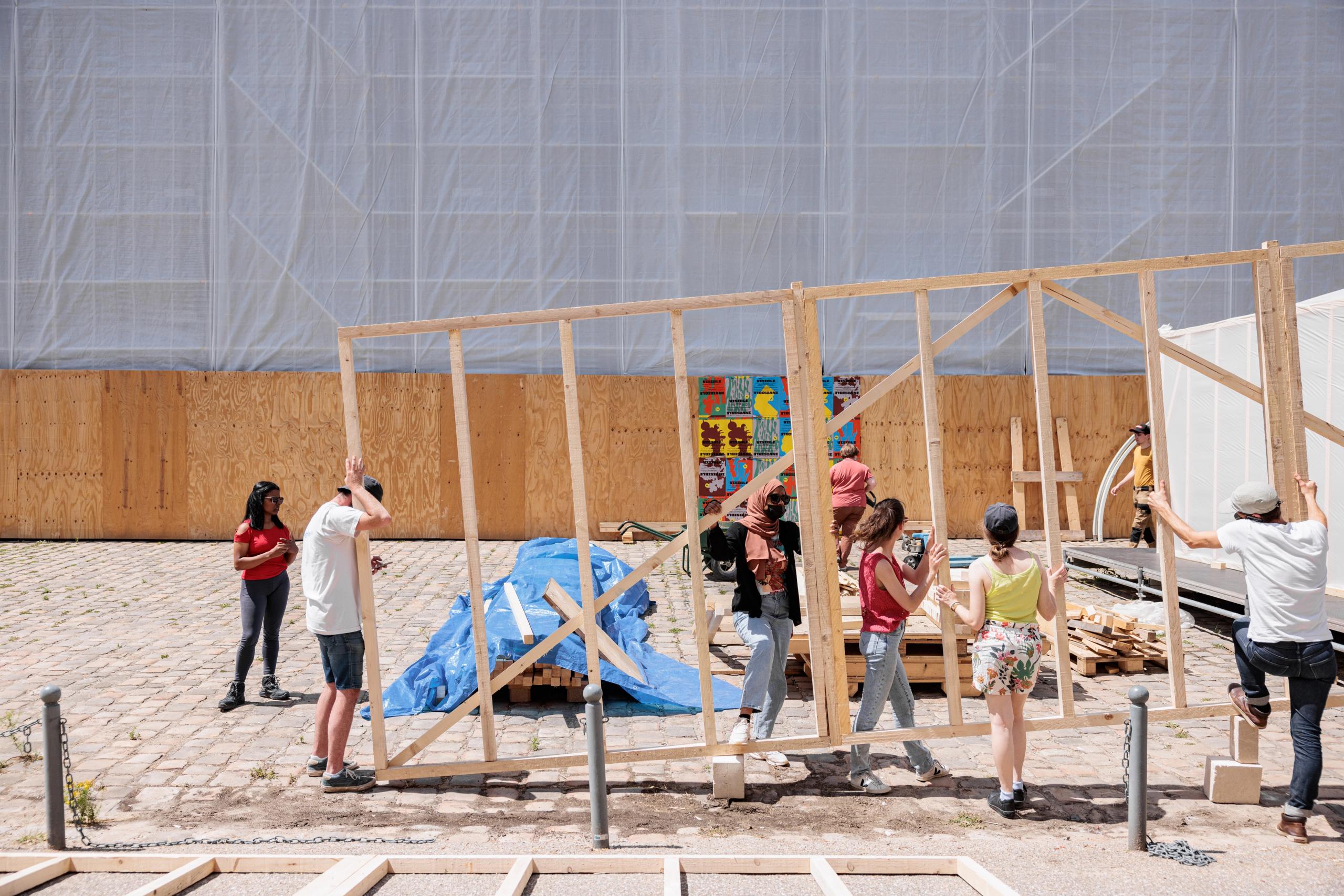 Workshop 60x60 à Versailles : montage collectif d’une ossature bois légère en panneaux manuportables, devant les façades bâchées de la Cour de la Maréchalerie.