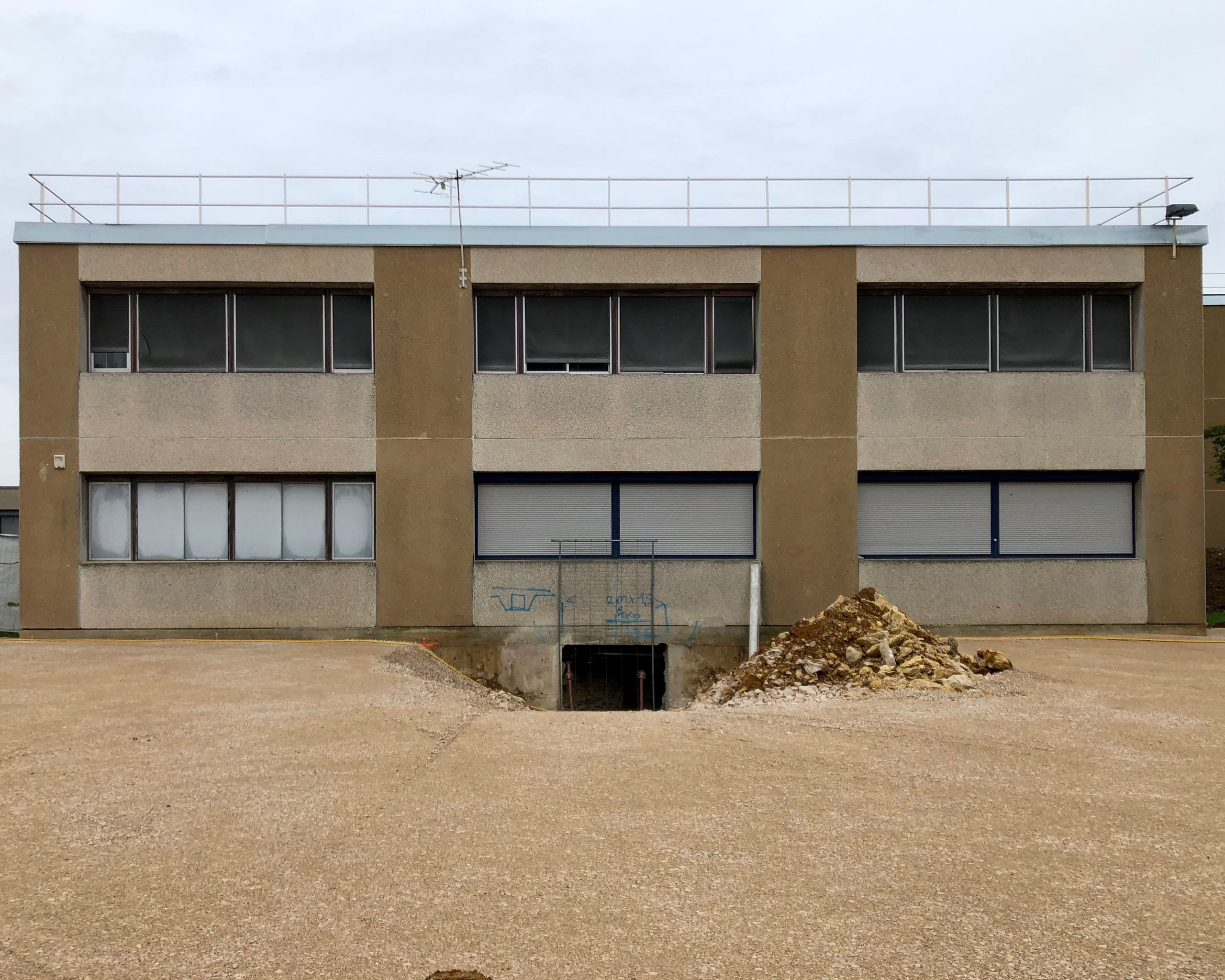 Façade existante du collège Maryse Bastié à Dole, volume années 70 en béton préfabriqué, trame rationnelle et accès en sous-sol en cours de restructuration.